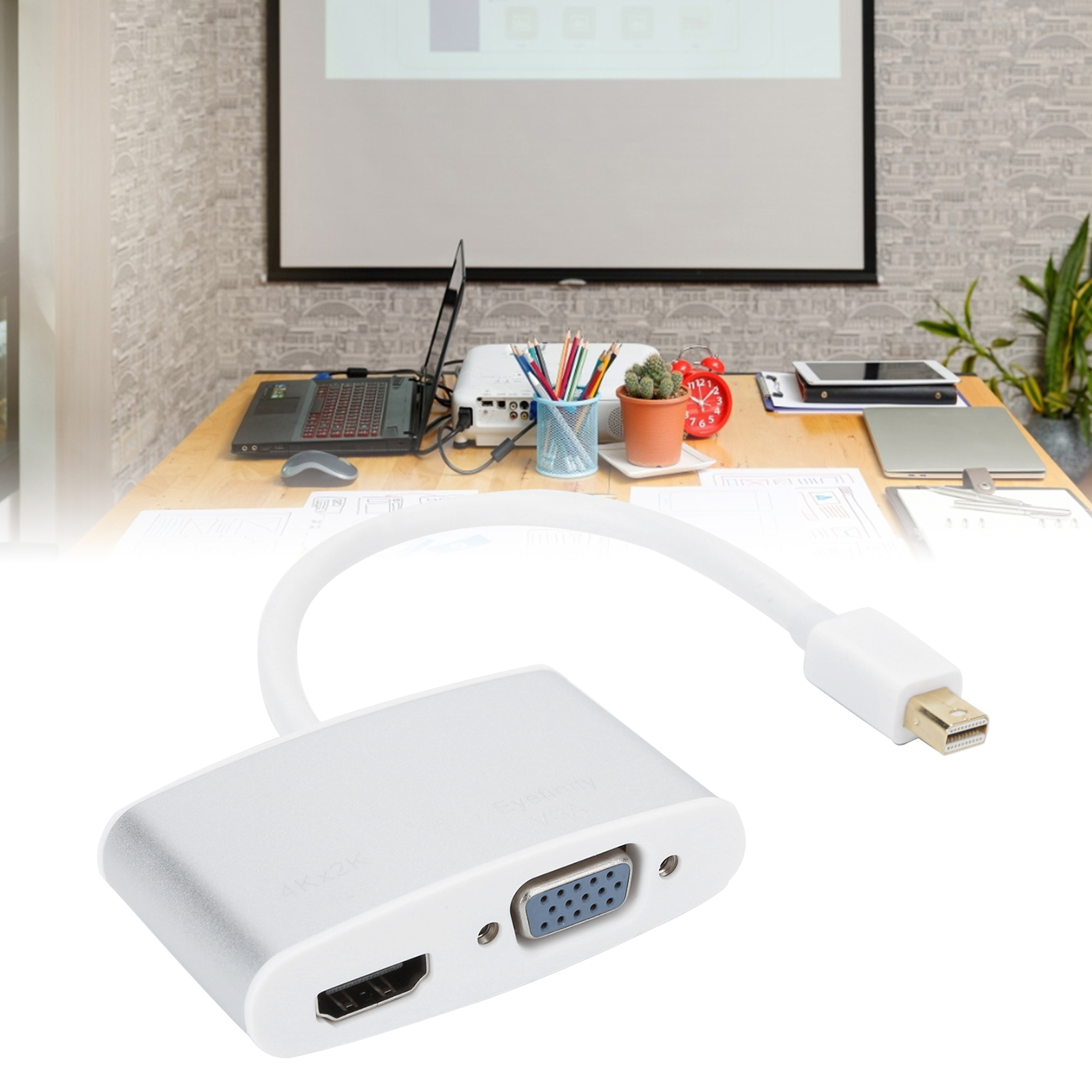 Ein silberner HDMI-zu-VGA-Adapter steht im Fokus. Im Hintergrund befinden sich ein Laptop, ein Projektor und Büromaterial.
