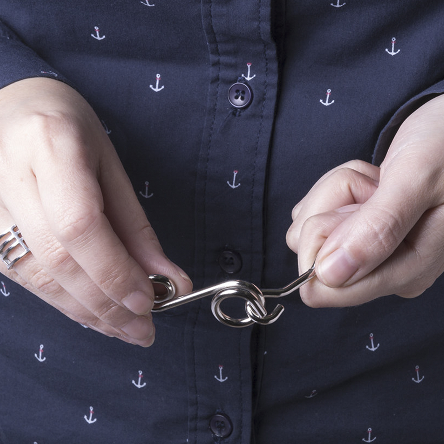 Mani che tengono un puzzle di metallo argentato contro una camicia blu navy con motivi di ancore bianche. Un anello è sulla mano sinistra.