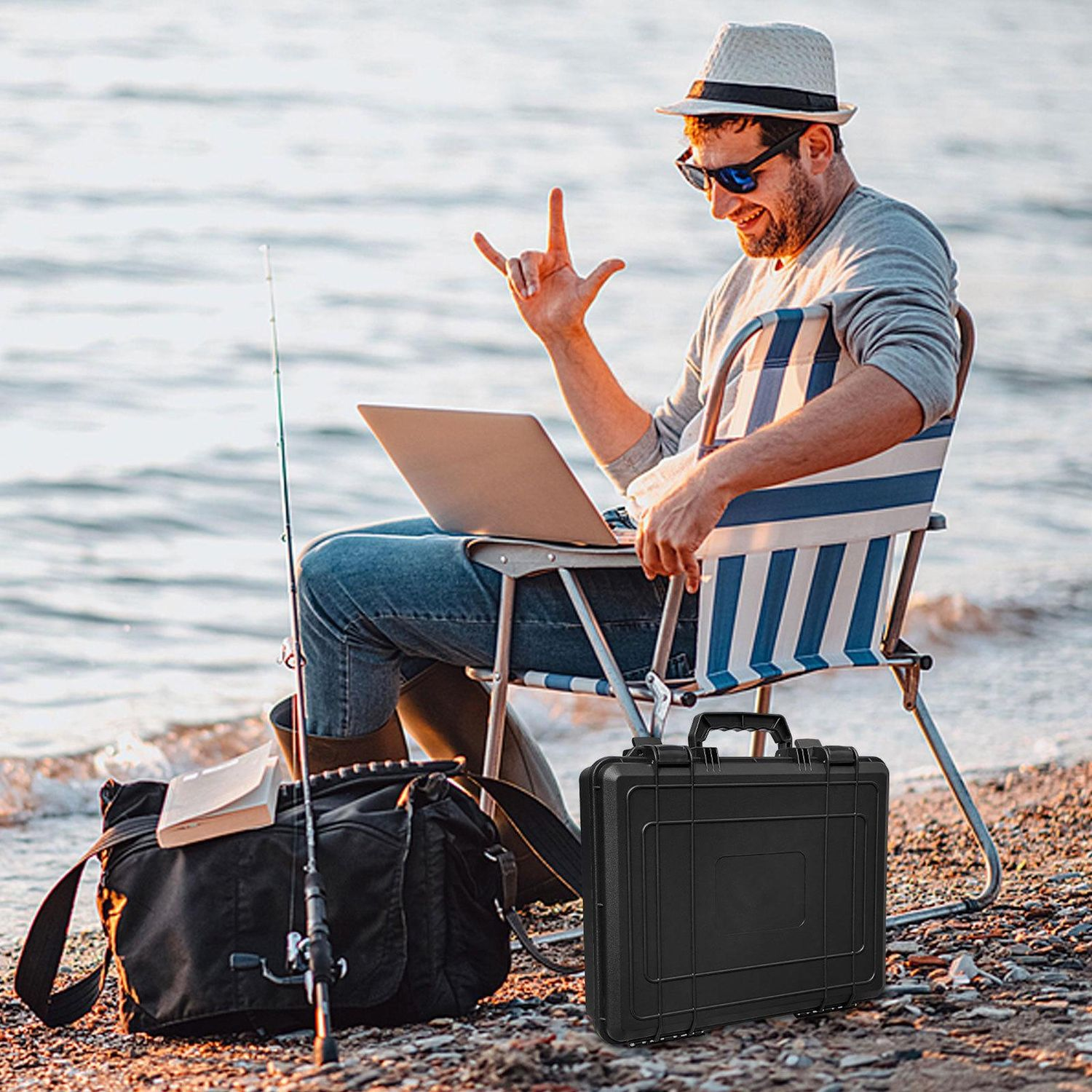 Uomo sulla spiaggia con laptop, sedia, canna da pesca, borsa nera e valigetta. Sta facendo un gesto rock.