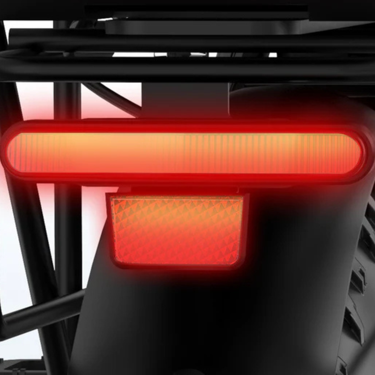 Zbliżenie tylnego światła i odblasku roweru, oba świecą na czerwono. Światło jest długie i prostokątne, odblask poniżej.