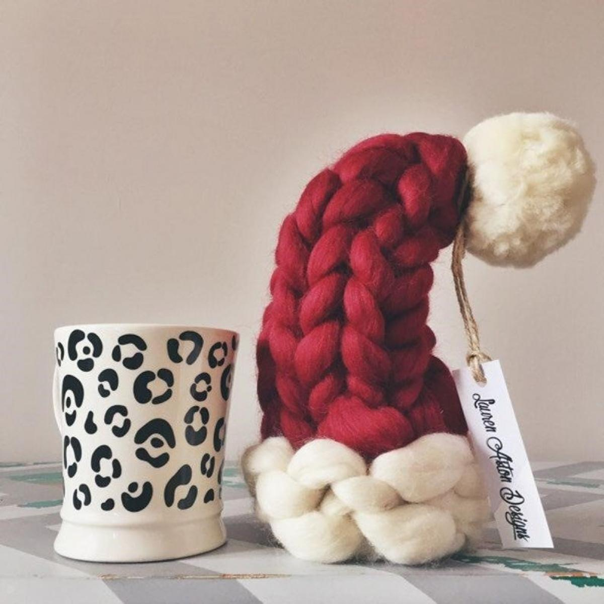 Eine rot-weiße Strickmütze mit weißem Bommel neben einer weißen Tasse mit schwarzen Leopardenflecken.