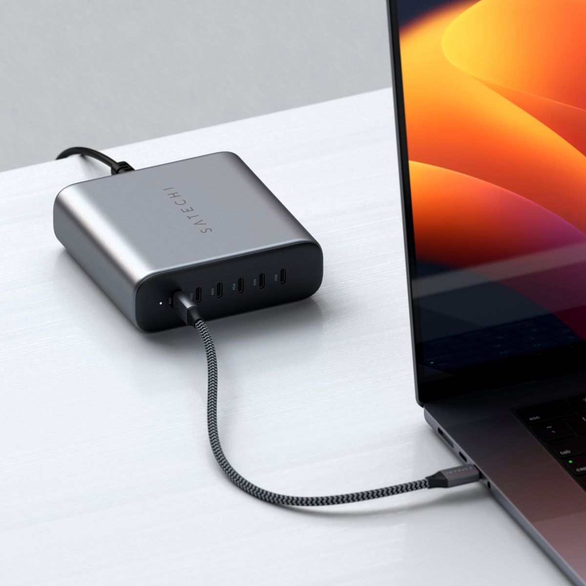Un hub Satechi grigio è collegato a un laptop. L'hub ha più porte. Lo schermo del laptop mostra una sfumatura arancione e rossa.