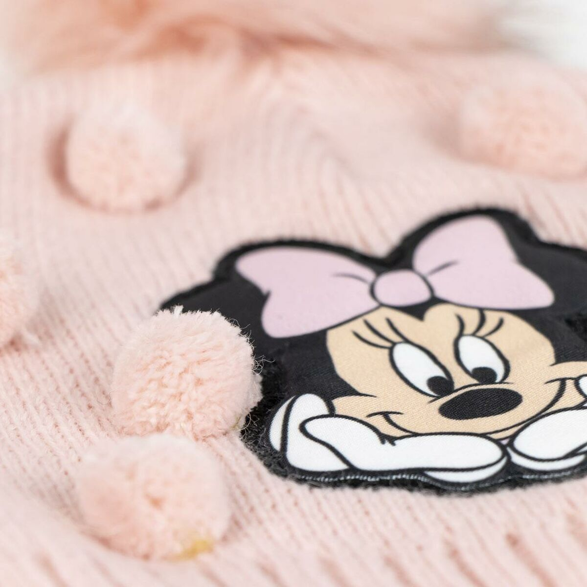 Rosa Strickmütze mit Minnie-Maus-Aufnäher und Bommeln. Minnie hat eine rosa Schleife. Weiche, flauschige Textur.