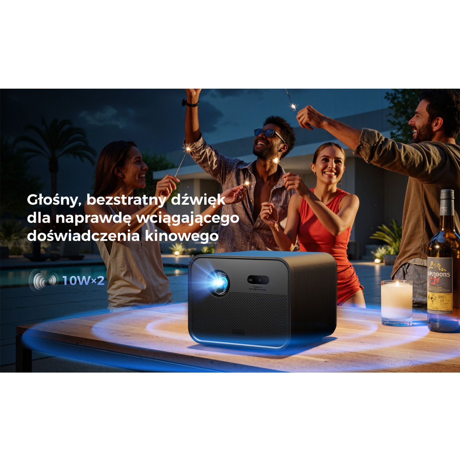 Ludzie trzymający zimne ognie wokół projektora. Na stole znajduje się projektor, świeca i butelka. Tekst promuje wciągający dźwięk.