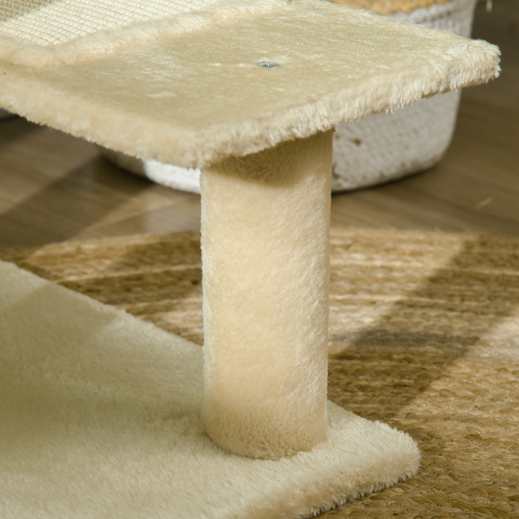 Un árbol para gatos beige con un poste y plataforma esponjosos, sobre una alfombra tejida. Una cesta blanca en el fondo.