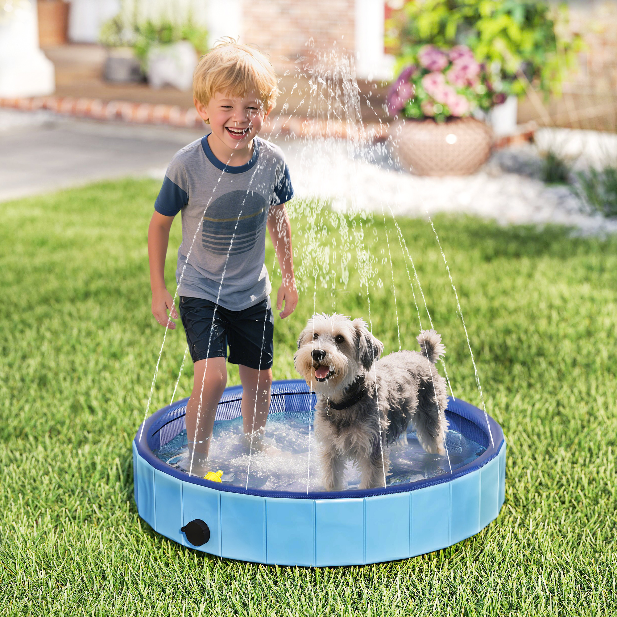 Un niño y un perro juegan en una piscina azul sobre césped. El agua salpica y el niño sonríe. Una casa está al fondo.