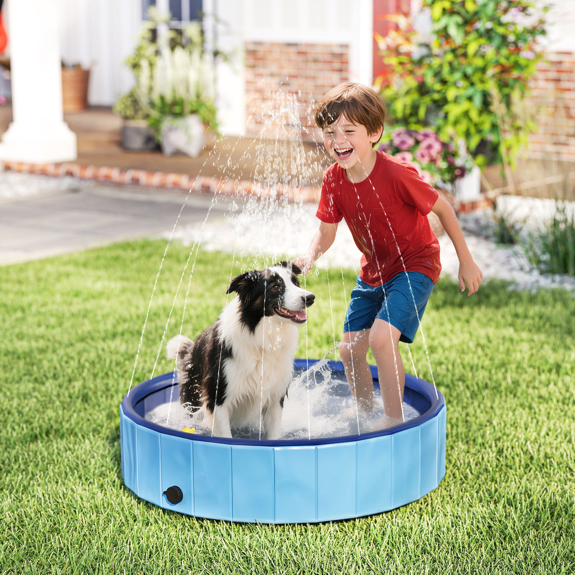 Un niño y un perro juegan en una piscina azul con agua rociada. El niño usa camisa roja y pantalones cortos azules. El perro es blanco y negro.