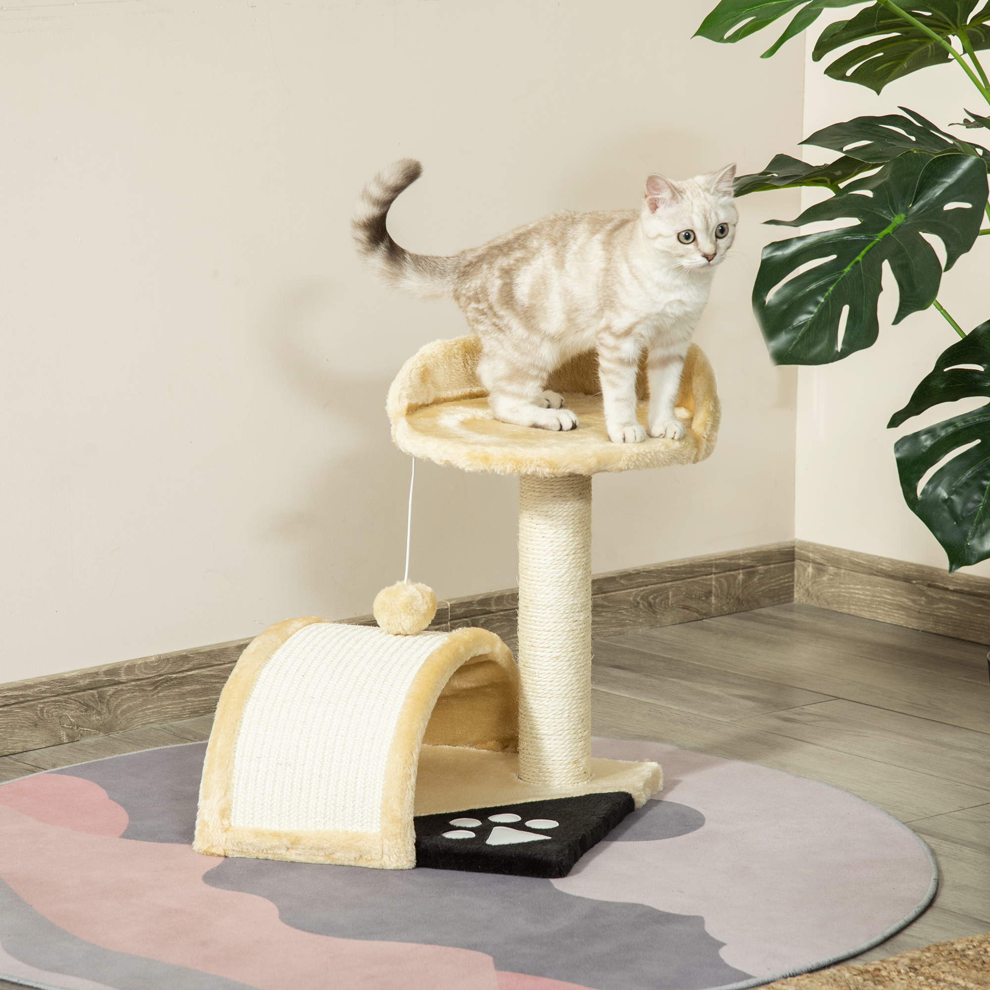 Un gato está de pie en un rascador beige. El árbol tiene un poste para rascar, una plataforma y un juguete. Una planta de Monstera está al fondo.