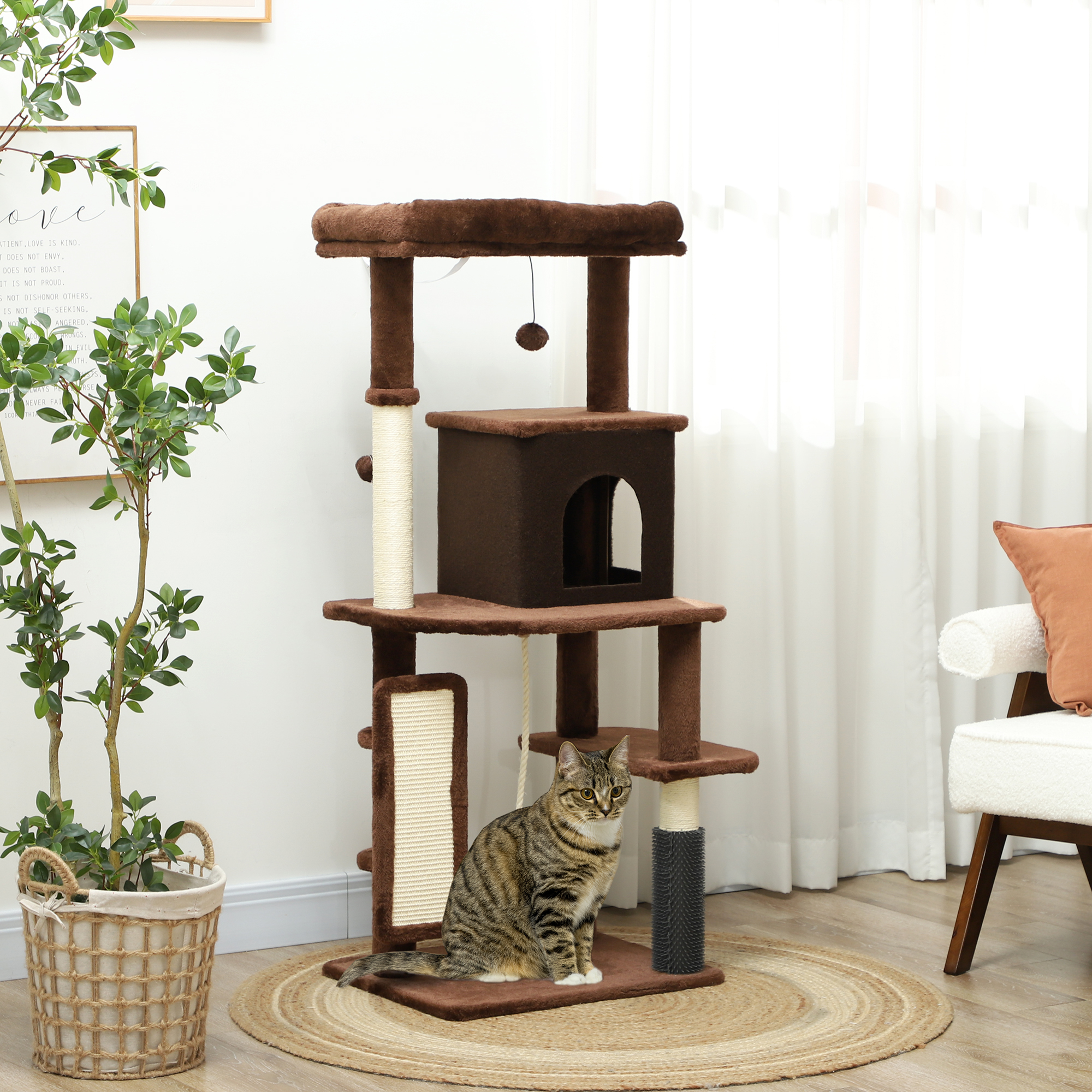 Un gato está sentado en un árbol para gatos marrón. El árbol tiene varios niveles, un poste para rascar y un juguete colgante. Hay una planta a la izquierda.
