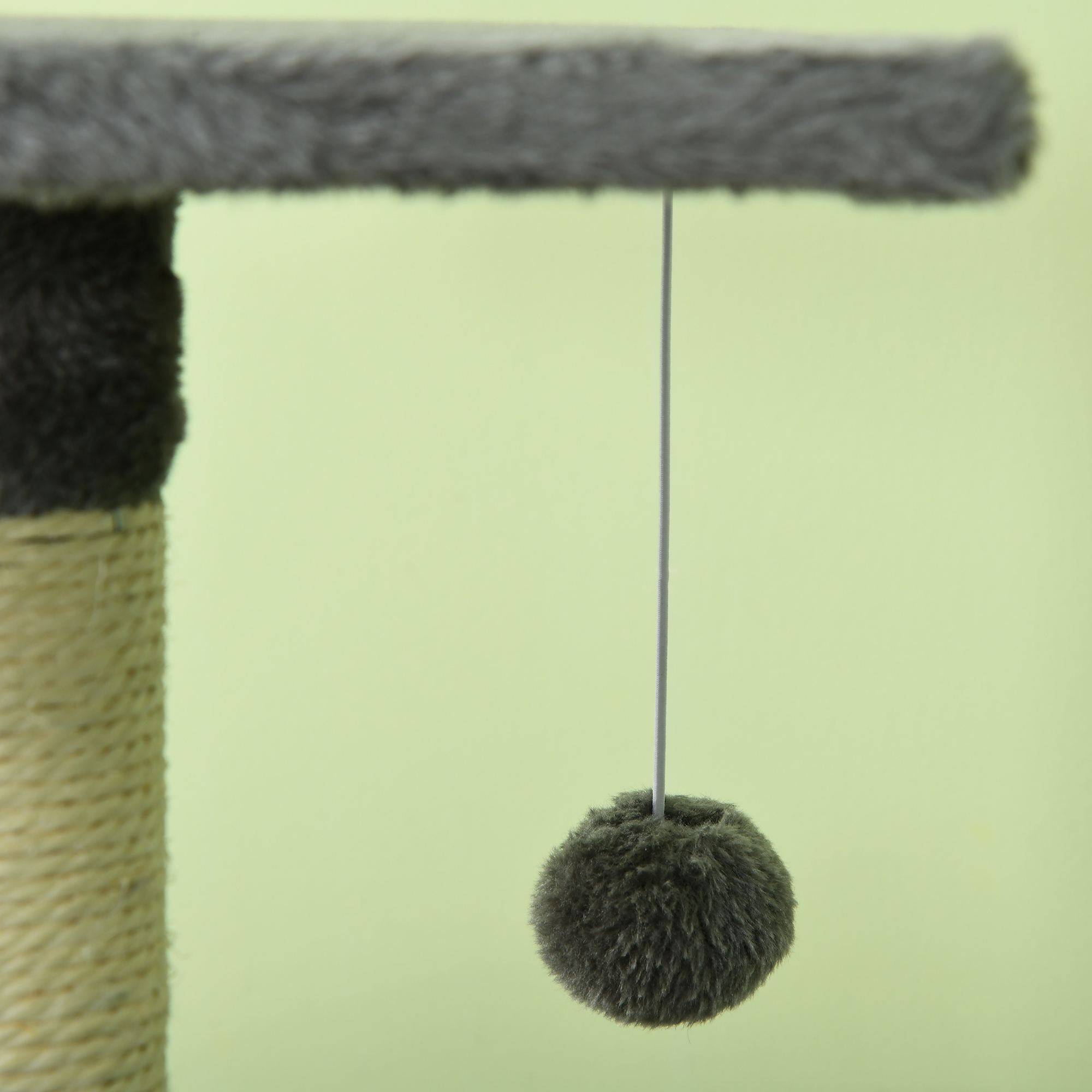 Un rascador con una bola gris y esponjosa colgando de una plataforma. El fondo es verde claro.