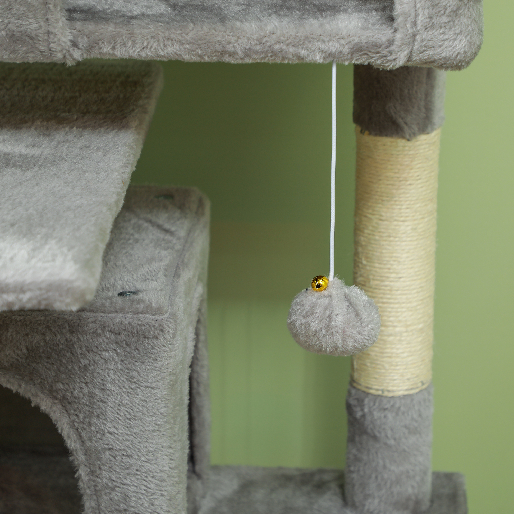 Un árbol para gatos gris con un juguete colgante. El fondo es verde claro. El juguete es gris con una campana dorada.