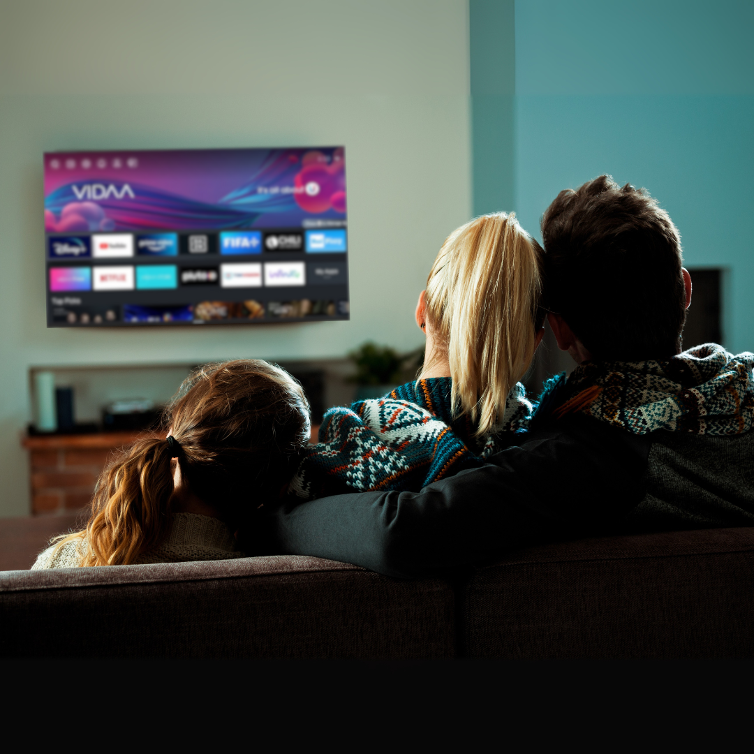 Famille de trois regardant la télévision. Ils sont assis sur un canapé. La télévision affiche une interface de streaming.