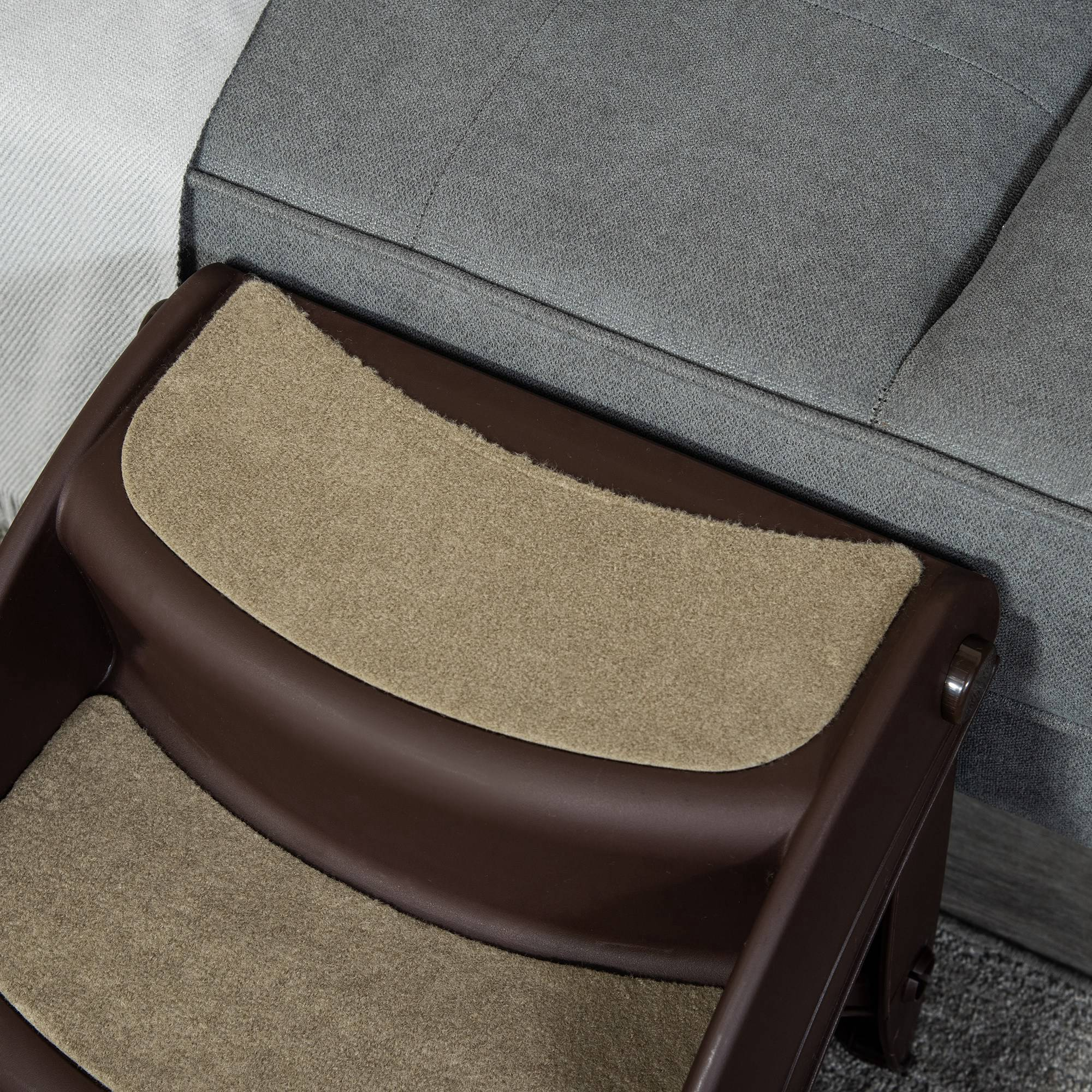 Una escalera marrón para mascotas está colocada cerca de un sofá gris. Los escalones están cubiertos de moqueta beige.