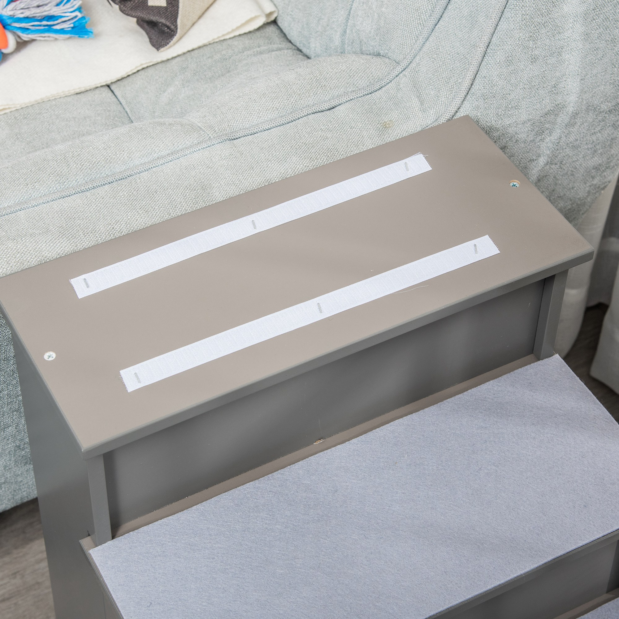 Escalera para mascotas de dos escalones. El escalón superior tiene tiras de velcro. Un sofá gris claro está al fondo.