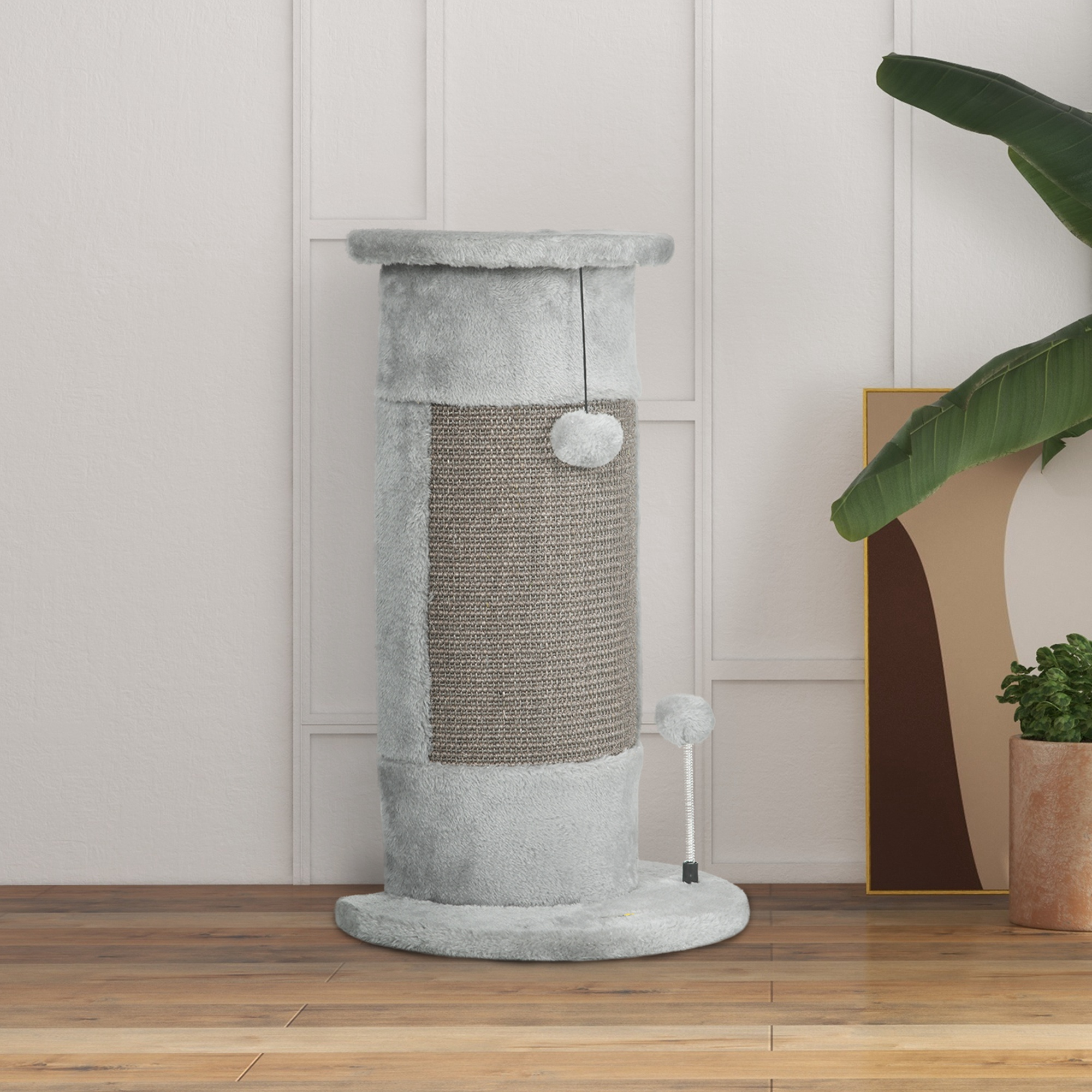 Un rascador gris para gatos con centro de sisal, parte superior esponjosa y dos juguetes colgantes. Una planta y una obra de arte en el fondo.