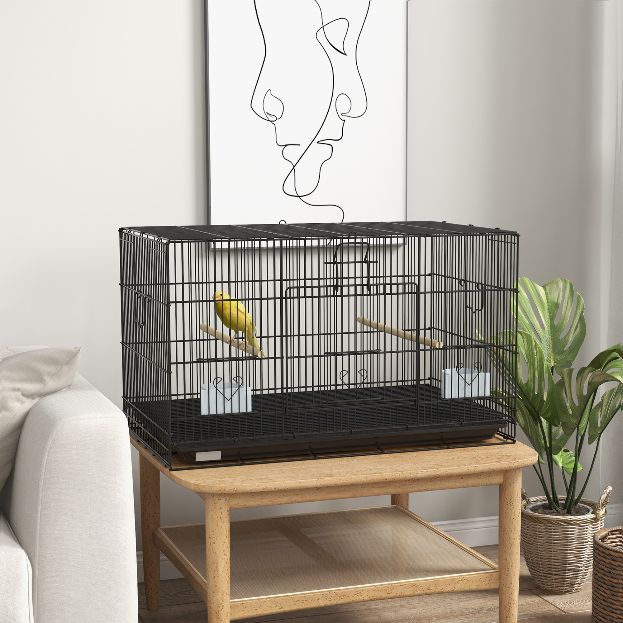 Una jaula negra con un pájaro amarillo dentro, sobre una mesa de madera. Una obra de arte minimalista cuelga en la pared. Hay plantas.