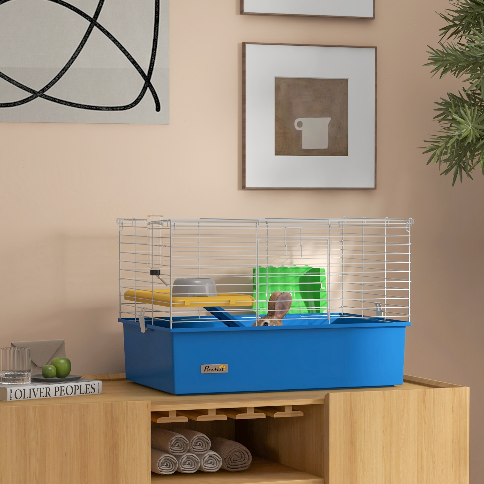 Una jaula azul con un hámster dentro, sobre un mueble de madera. Hay dos cuadros enmarcados y plantas encima.