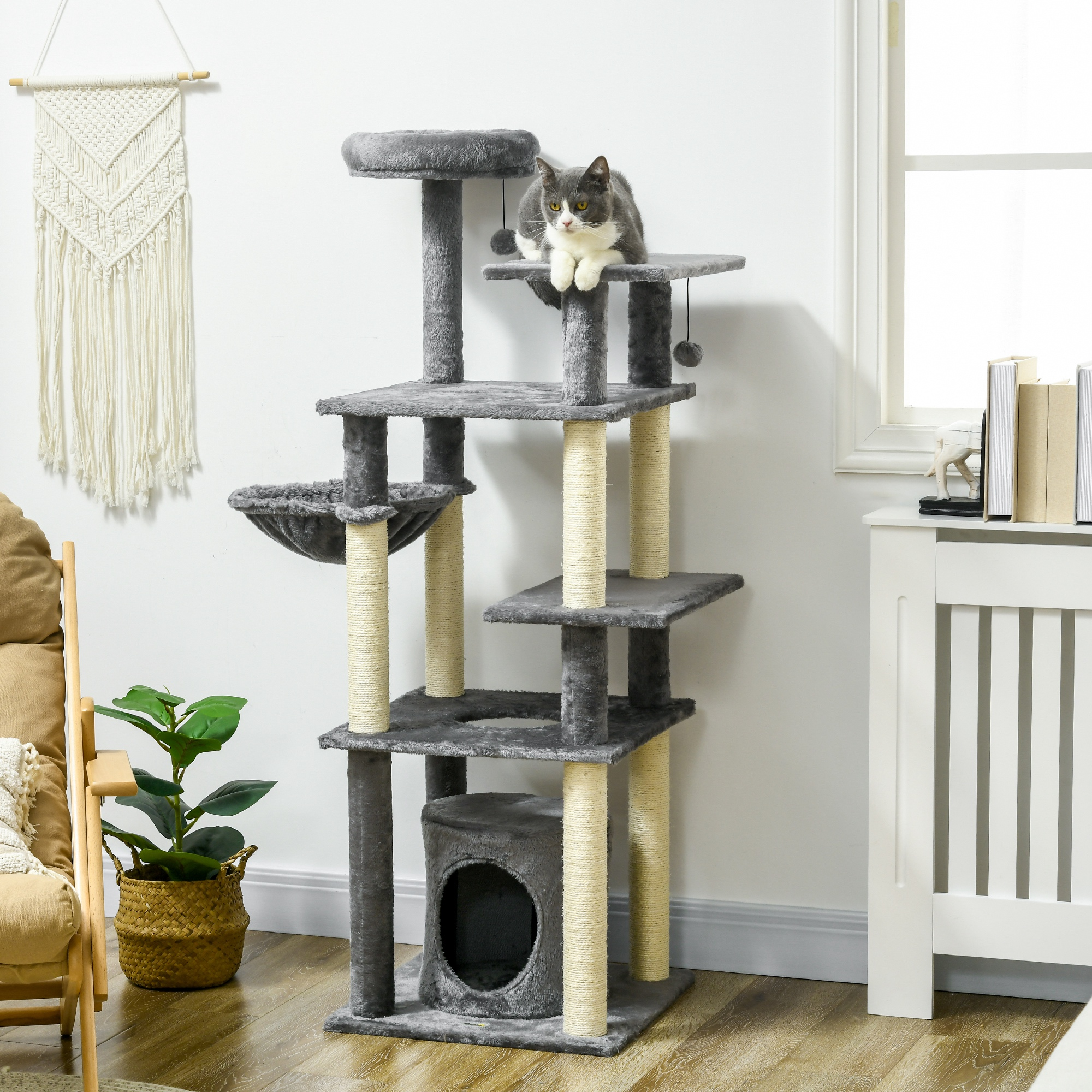 Un árbol para gatos con un gato gris encima. Tiene múltiples niveles, postes rascadores y una casa para gatos. Es visible un tapiz tejido.