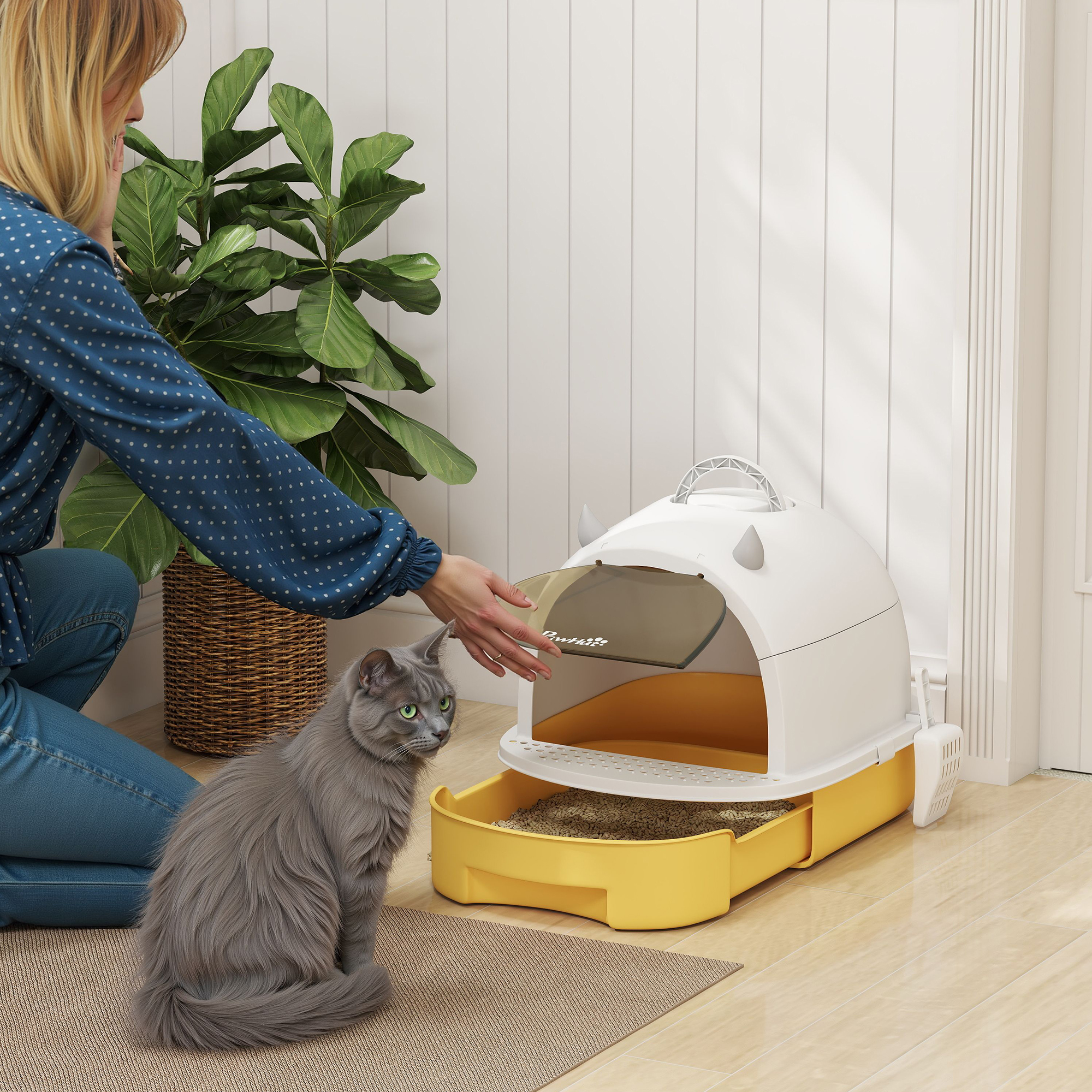 Una mujer junto a una caja de arena, un gato está sentado cerca. La caja es amarilla y blanca, con un gato a su lado.