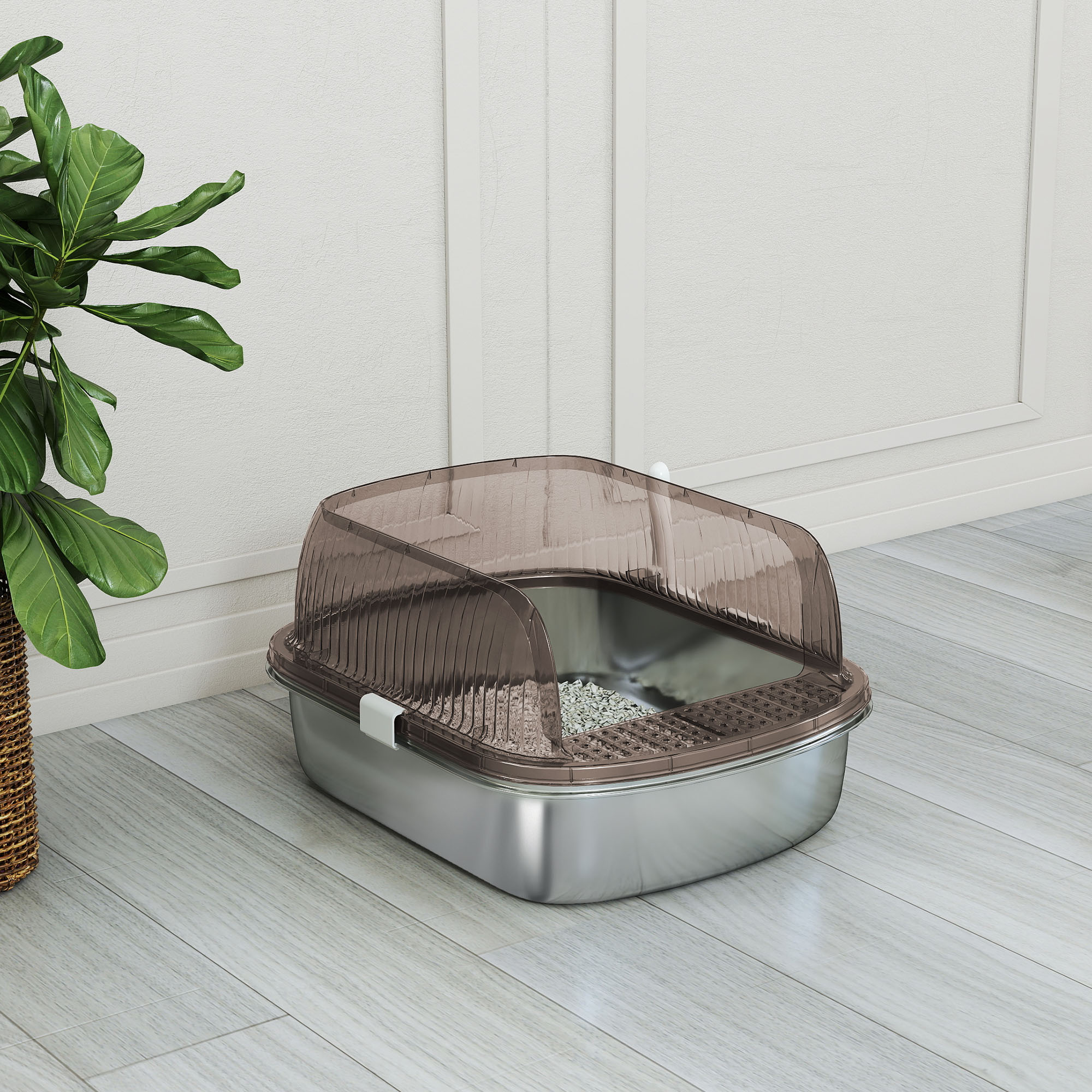 Una caja de arena para gatos con una cubierta transparente marrón se encuentra sobre un piso de madera clara. Una planta verde frondosa está a la izquierda.