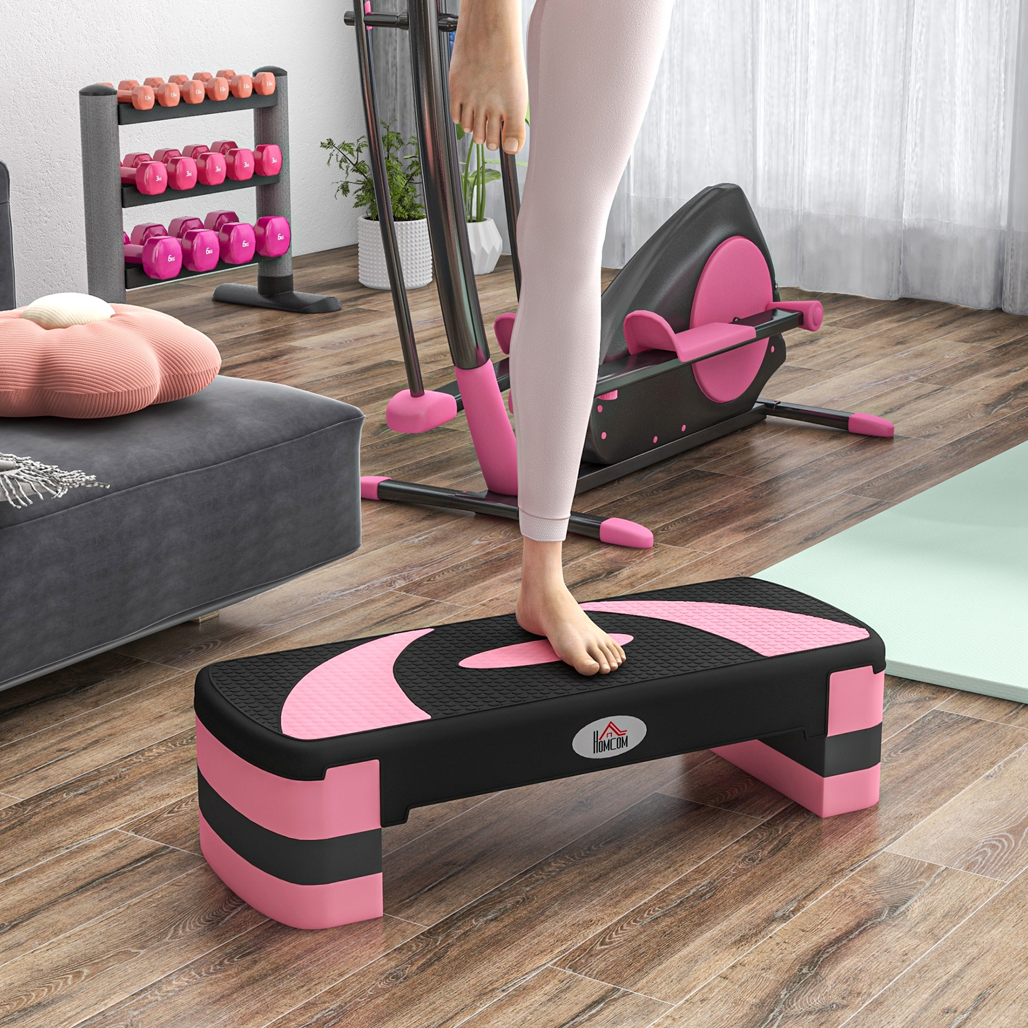 Una persona está de pie en una plataforma de step en un gimnasio en casa. Equipos y pesas están en el fondo.