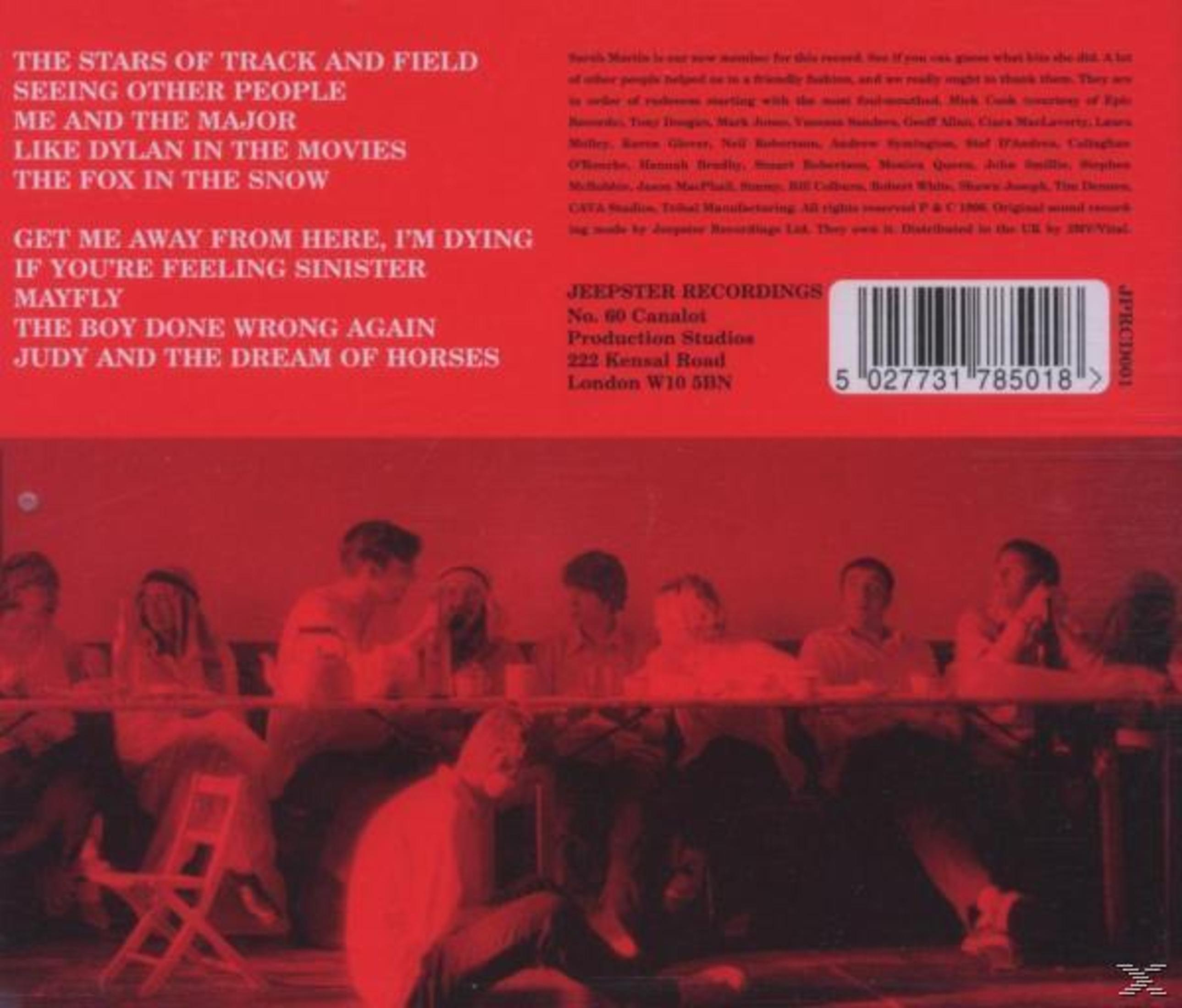Albumcover mit rotem Hintergrund und weißem Text. Im Hintergrund sind Menschen zu sehen. Im Vordergrund steht ein Stuhl.