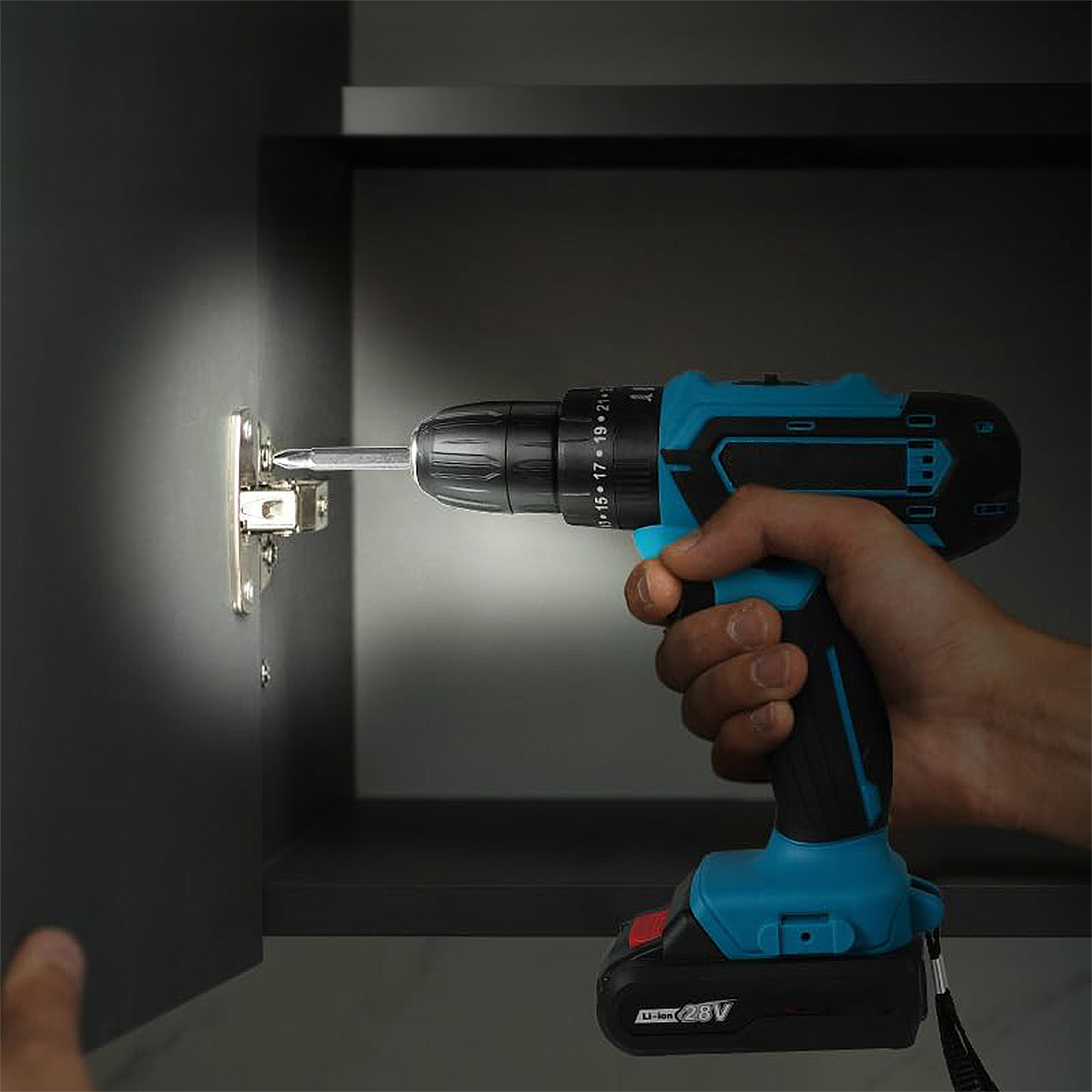 Una mano usa un trapano blu e nero per avvitare una cerniera dell'armadio. Lo sfondo mostra un armadio scuro e una mano.