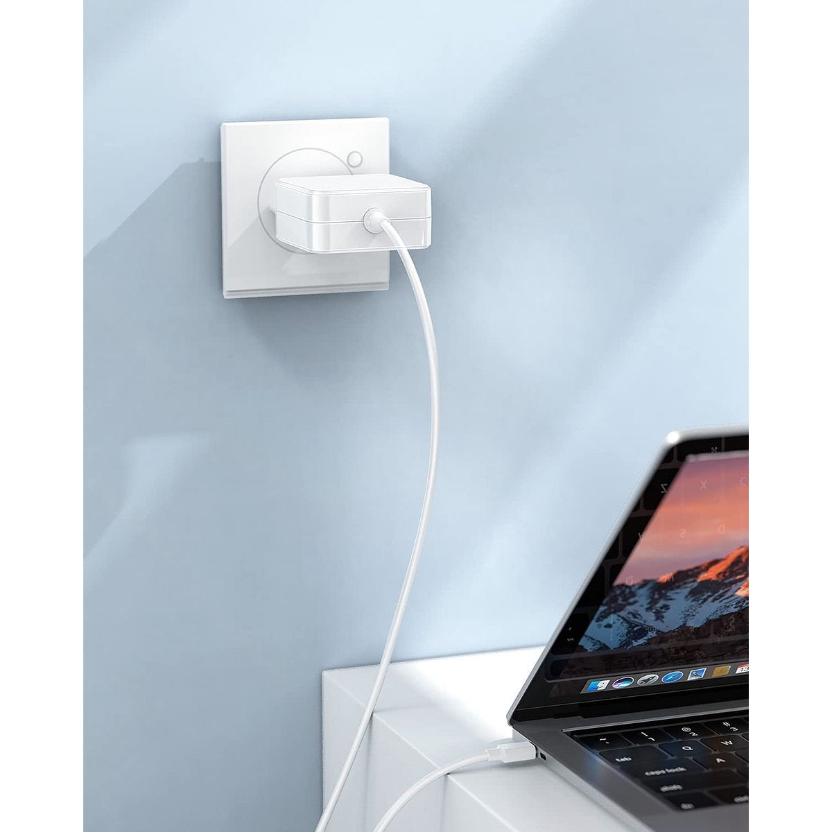 Een witte oplader is aangesloten op een stopcontact. Een witte kabel verbindt met een laptop.
