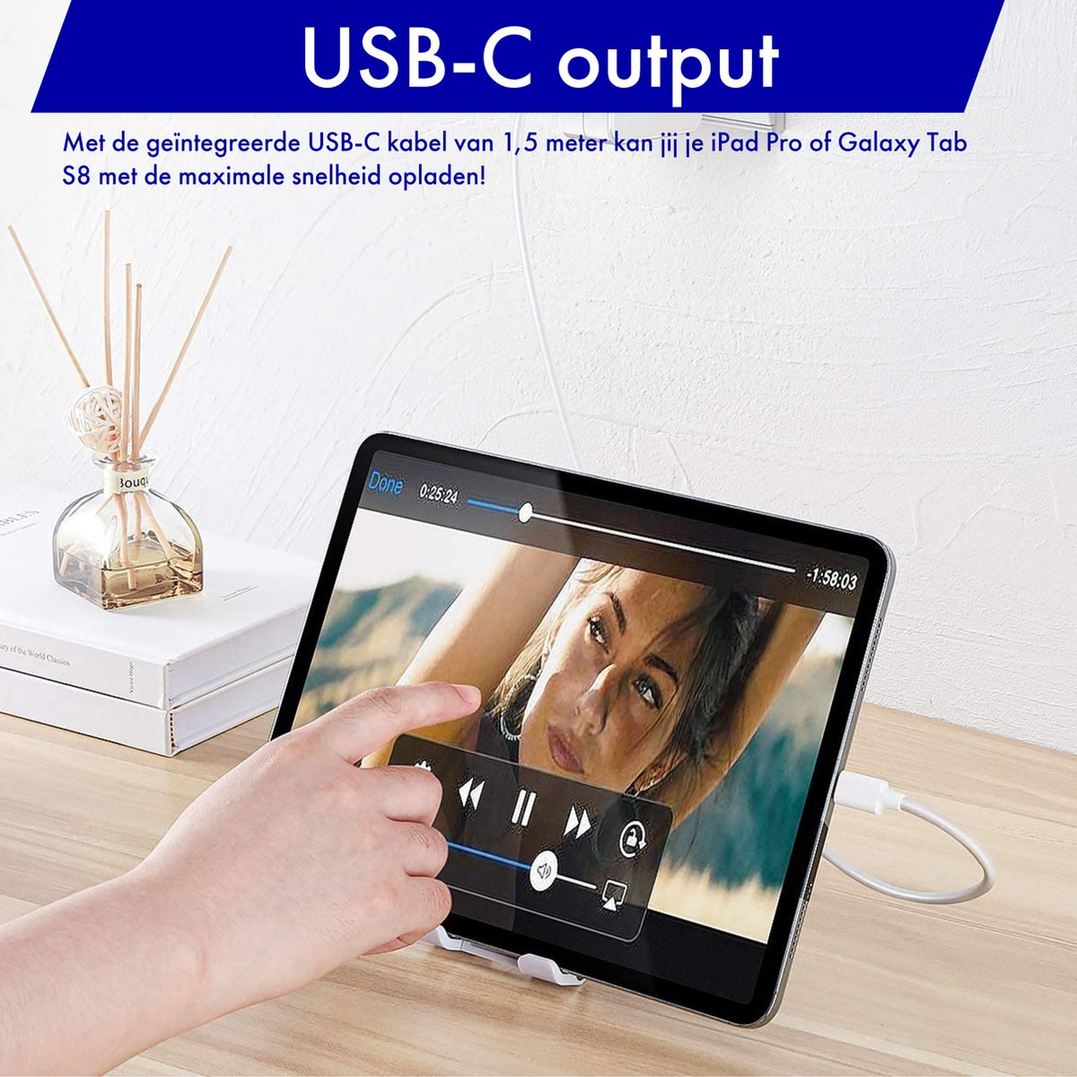 Een tablet is verbonden met een USB-C-kabel. Een hand wijst naar het scherm. Een diffuser en boeken liggen op tafel.