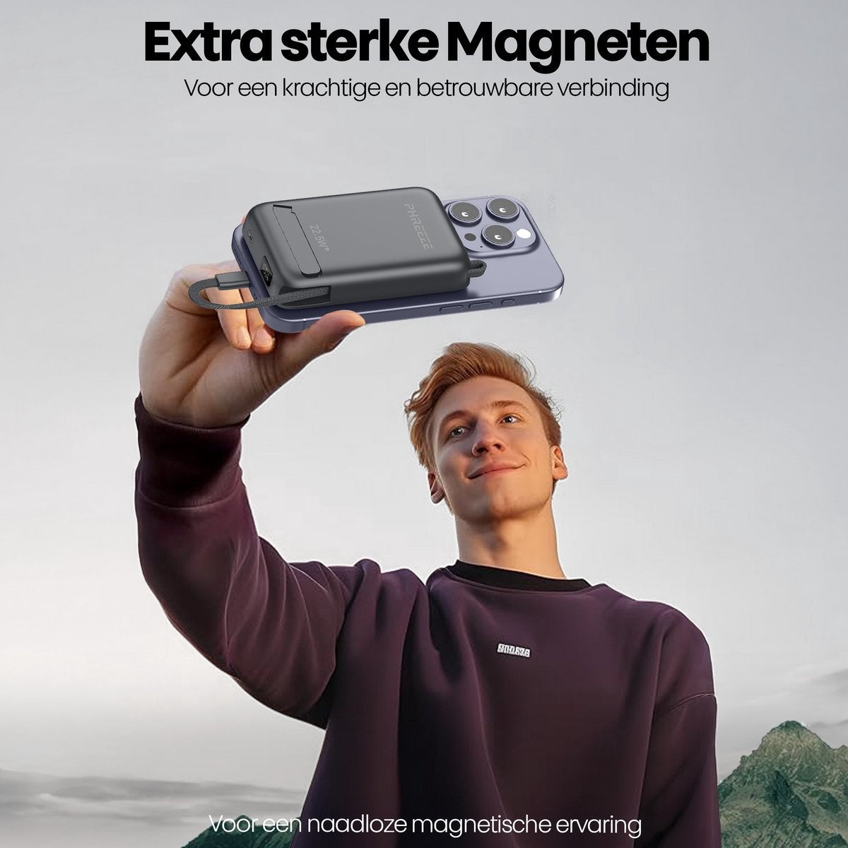 A person holds a phone with a magnetic charger attached in front of a mountain.