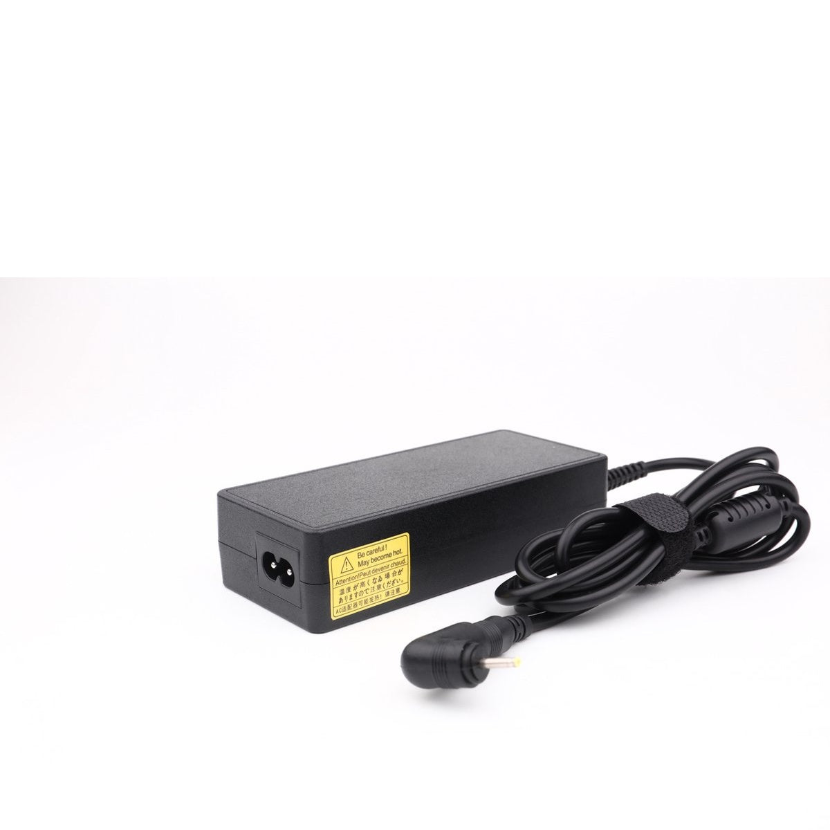 A black laptop power adapter with a warning label is on a white surface. The cable is coiled to the right. The power adapter is rectangular.