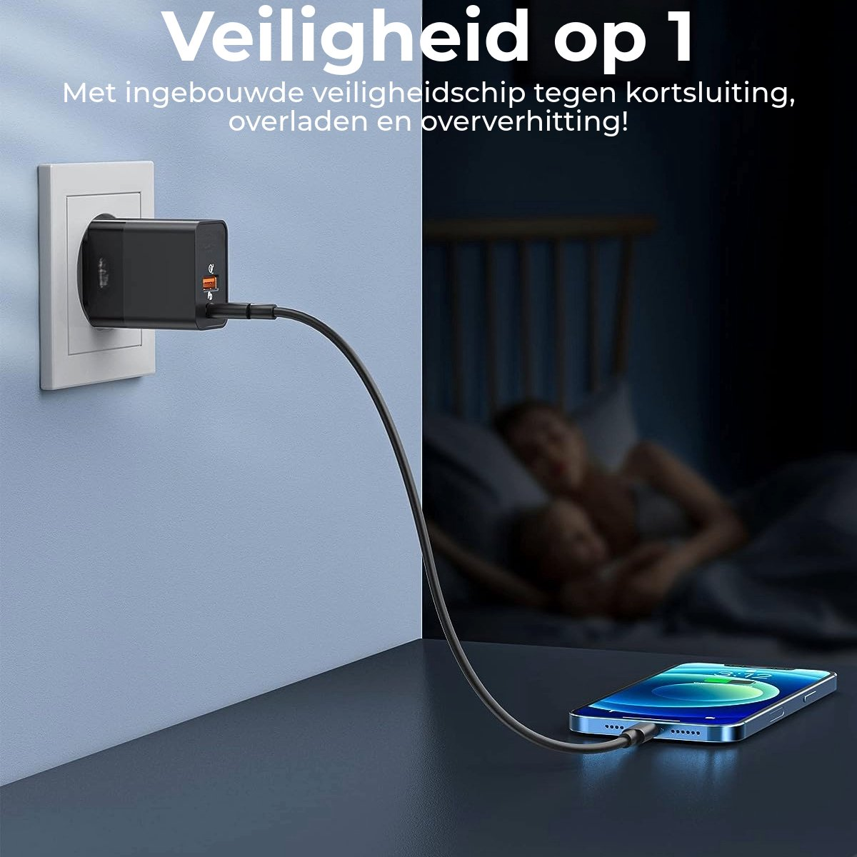 A black charger plugs into a wall outlet, connected to a phone on a table. A person is in bed in the blurred background.
