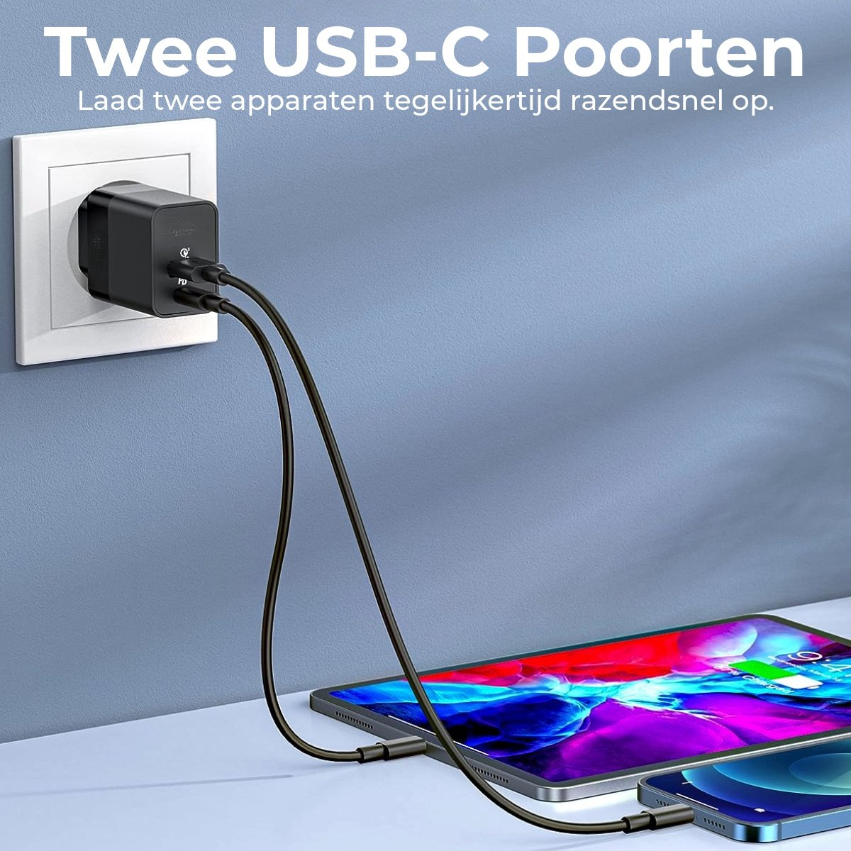 A black USB-C charger plugged into a wall, charging a tablet and a phone. The devices are on a white surface, against a blue wall.