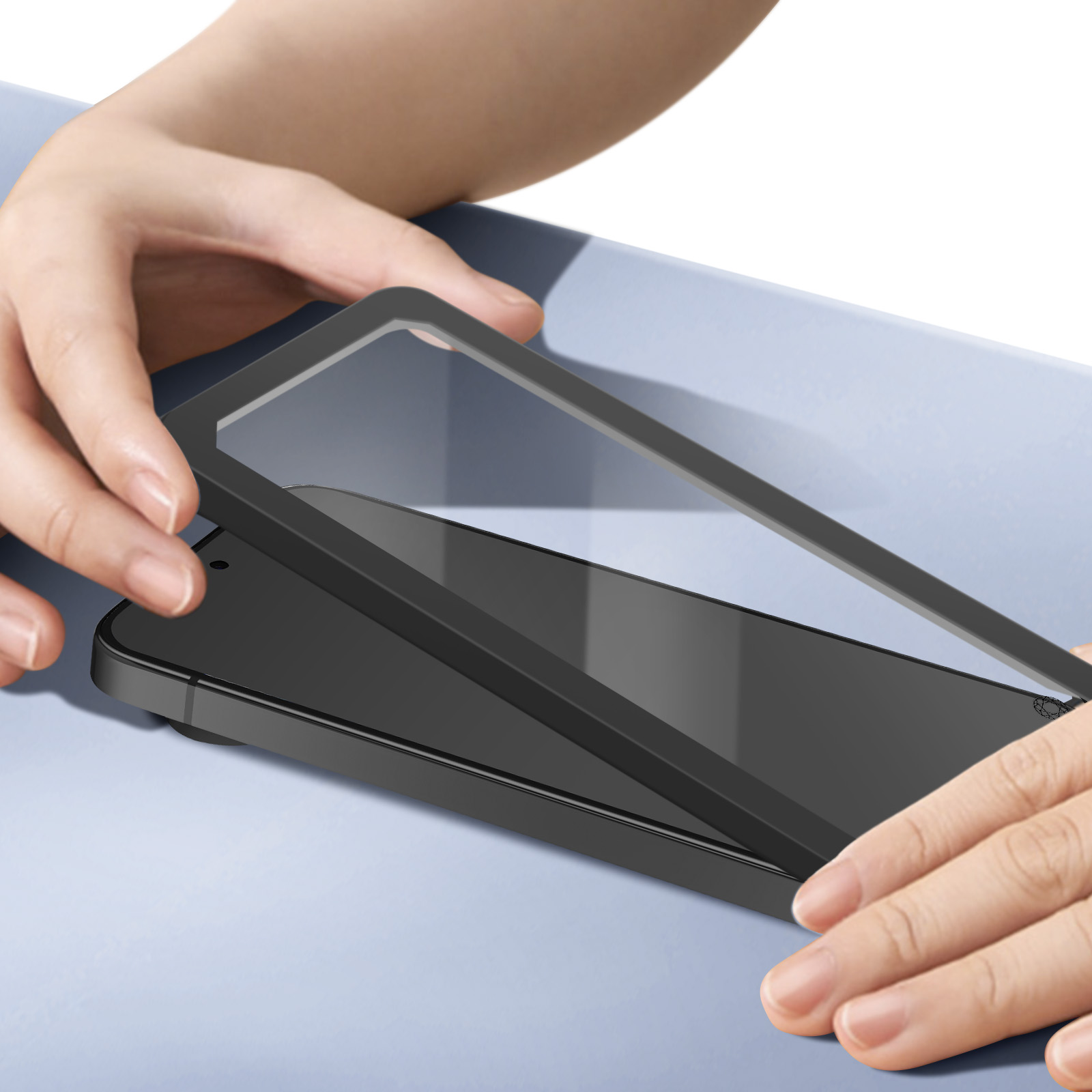 Mains tenant un protecteur d'écran transparent au-dessus d'un téléphone noir. Le téléphone est sur une surface bleu clair.