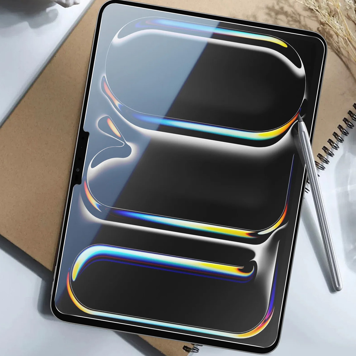 Un tablet con stilo è appoggiato su una scrivania. Lo schermo ha linee iridescenti. Un taccuino e una pianta sono sullo sfondo.