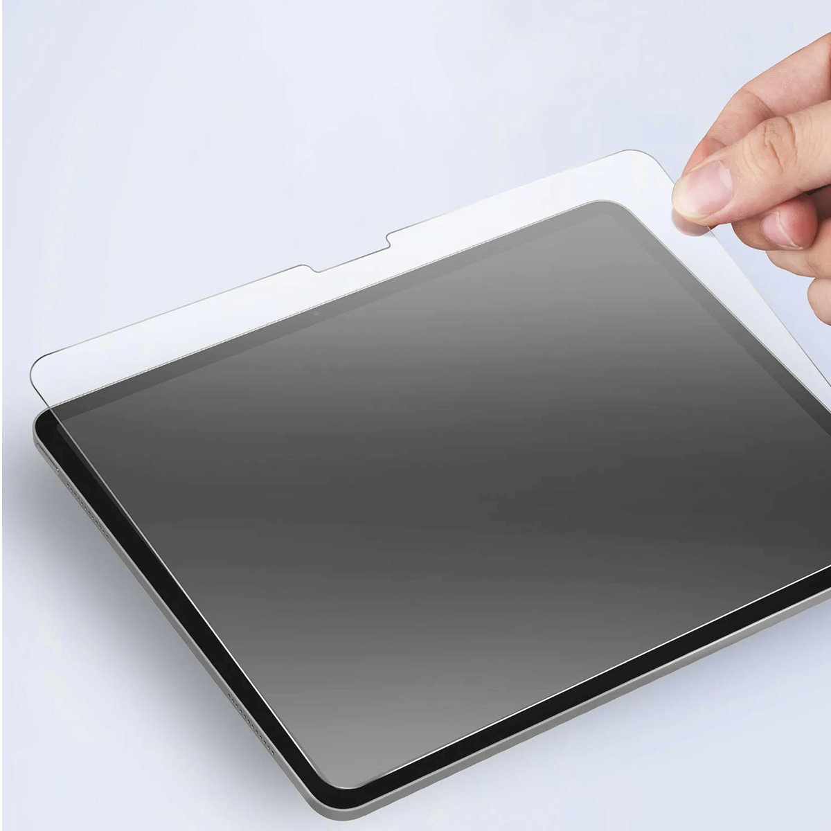 Une main pose un protecteur d'écran sur une tablette. La tablette est argentée, et l'écran est sombre.