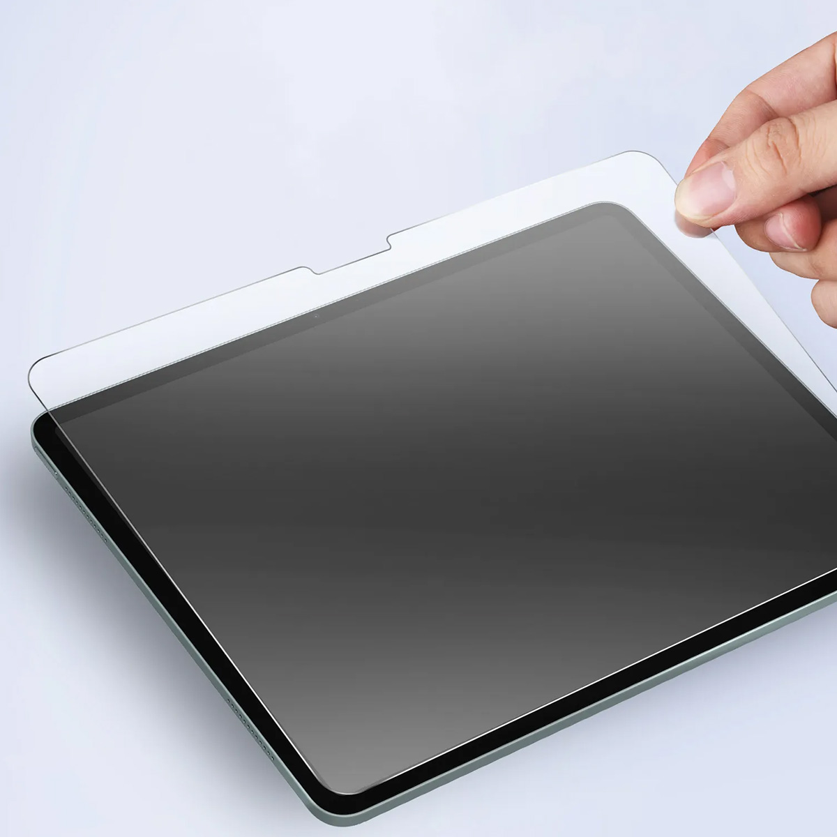 Une main tenant un protecteur d'écran au-dessus d'une tablette. La tablette est noire avec un bord vert et est posée sur une surface blanche.