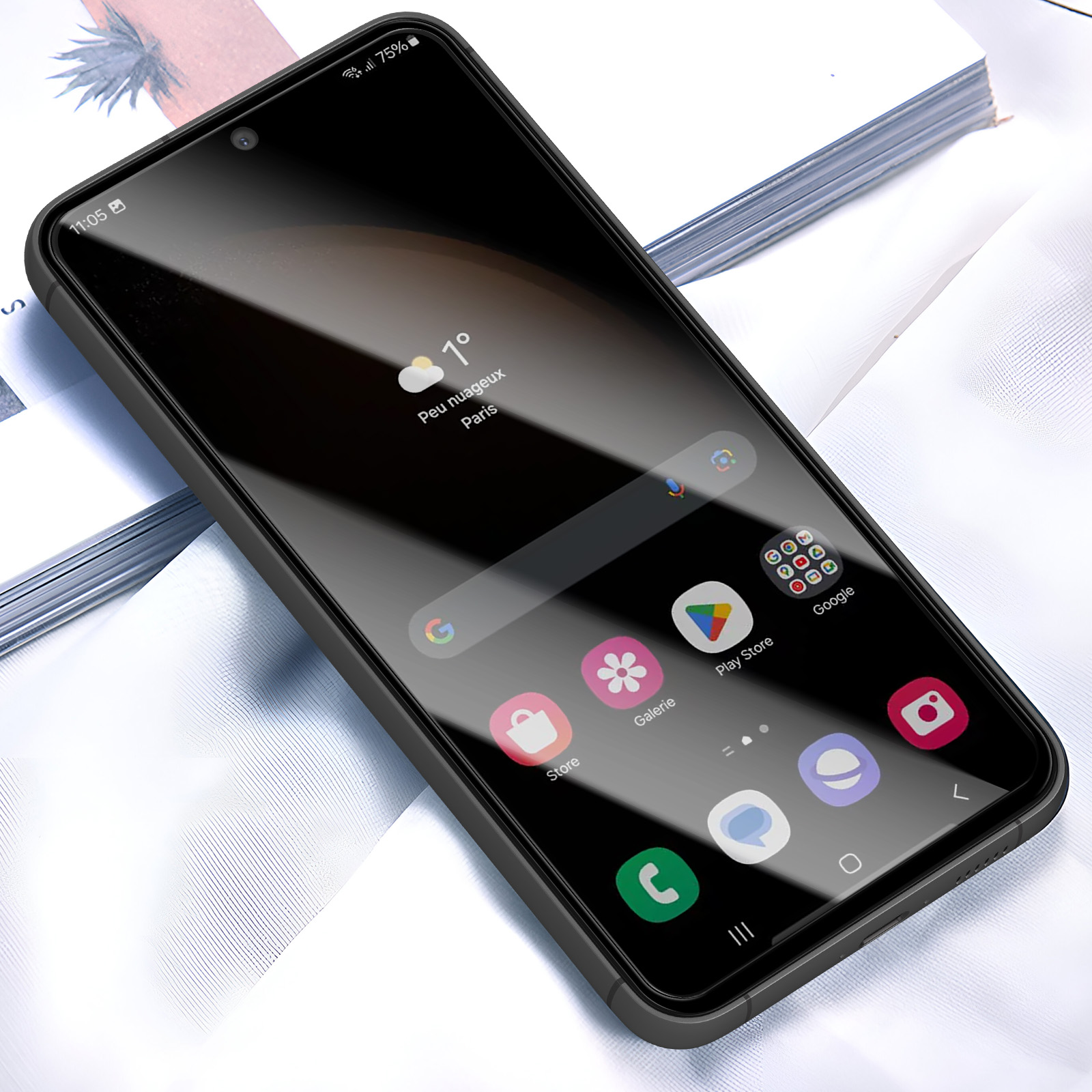 Uno smartphone con custodia nera mostra app e informazioni meteo. Poggia su una superficie bianca, con un libro sullo sfondo.