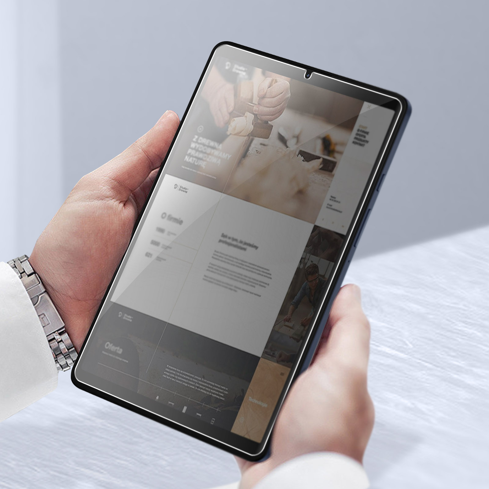 Mani che tengono un tablet che mostra un sito web con testo e immagini. Lo sfondo è una superficie chiara e sfocata.