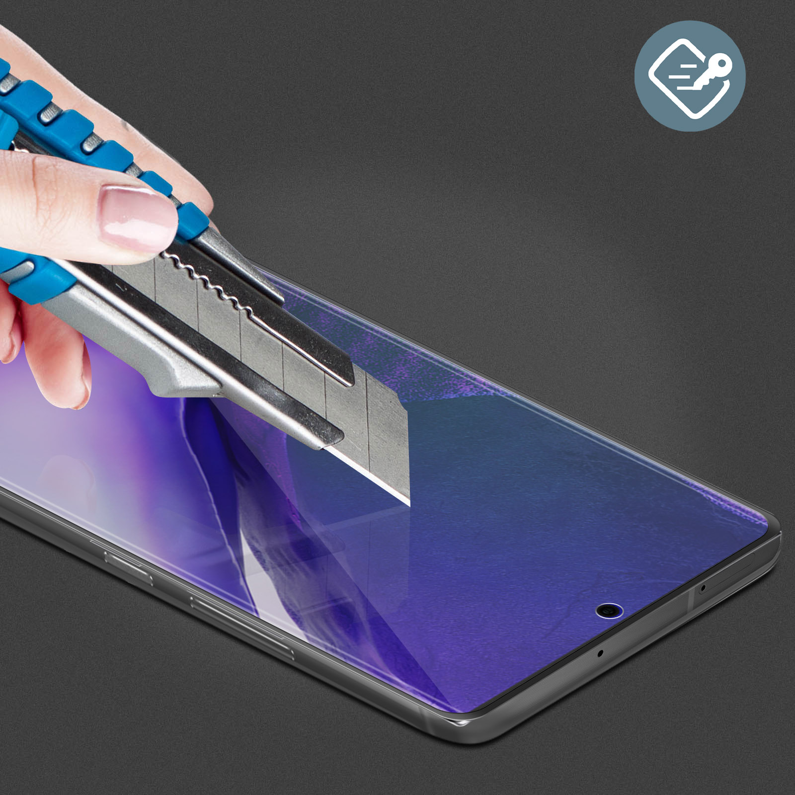 Une main utilise un cutter pour décoller un protecteur d'écran d'un smartphone. Le téléphone est sur une surface gris foncé.