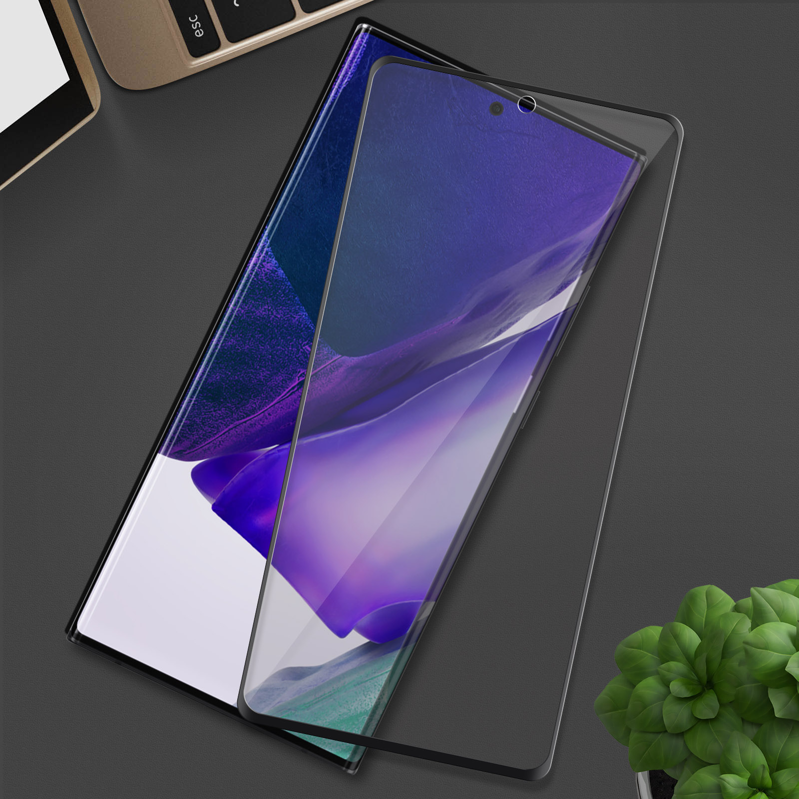 Un protecteur d'écran est sur un téléphone, sur une table. Un ordinateur portable et une petite plante sont en arrière-plan.