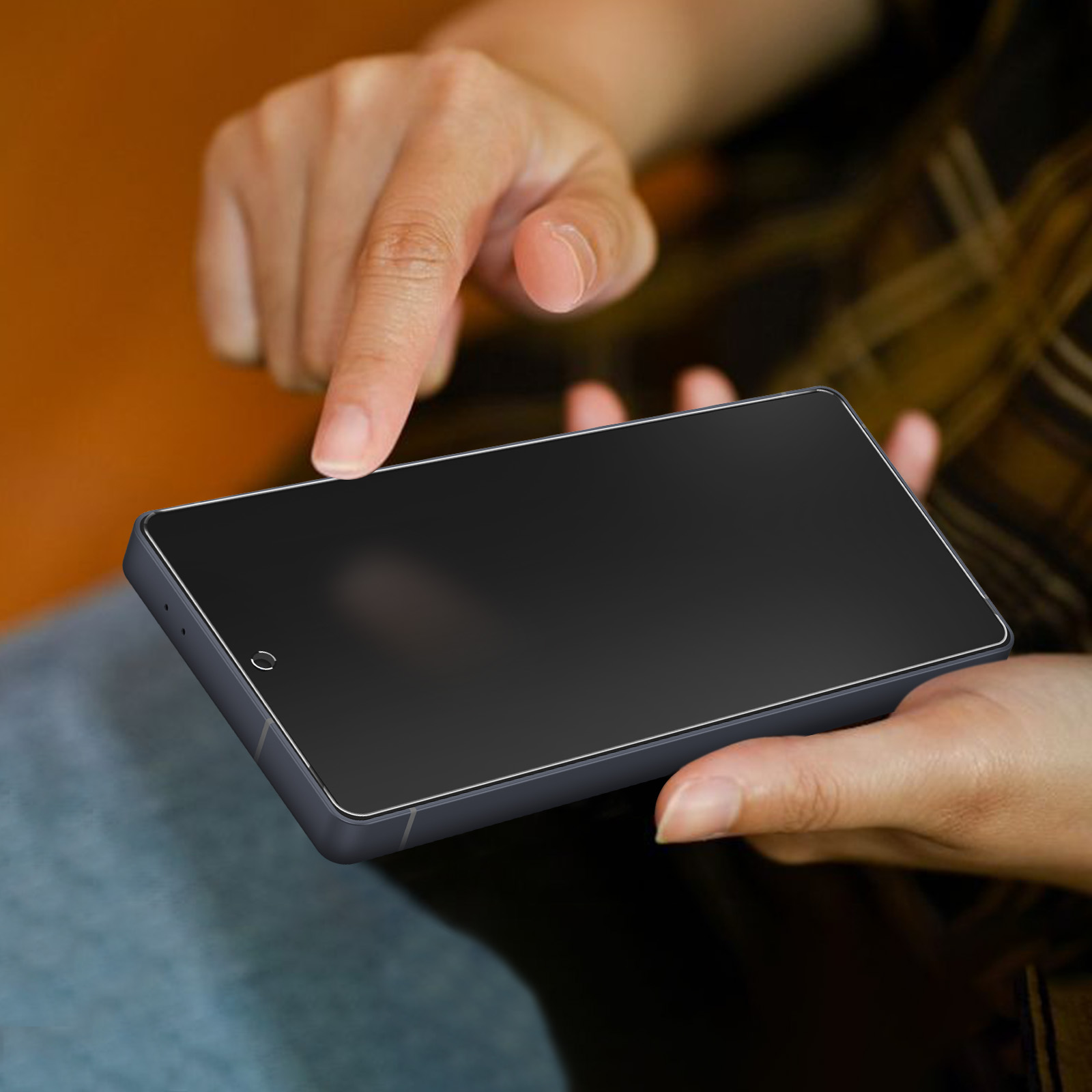 Le mani di una persona tengono un tablet grigio scuro. Un dito tocca lo schermo. Lo sfondo è sfocato, arancione e marrone.
