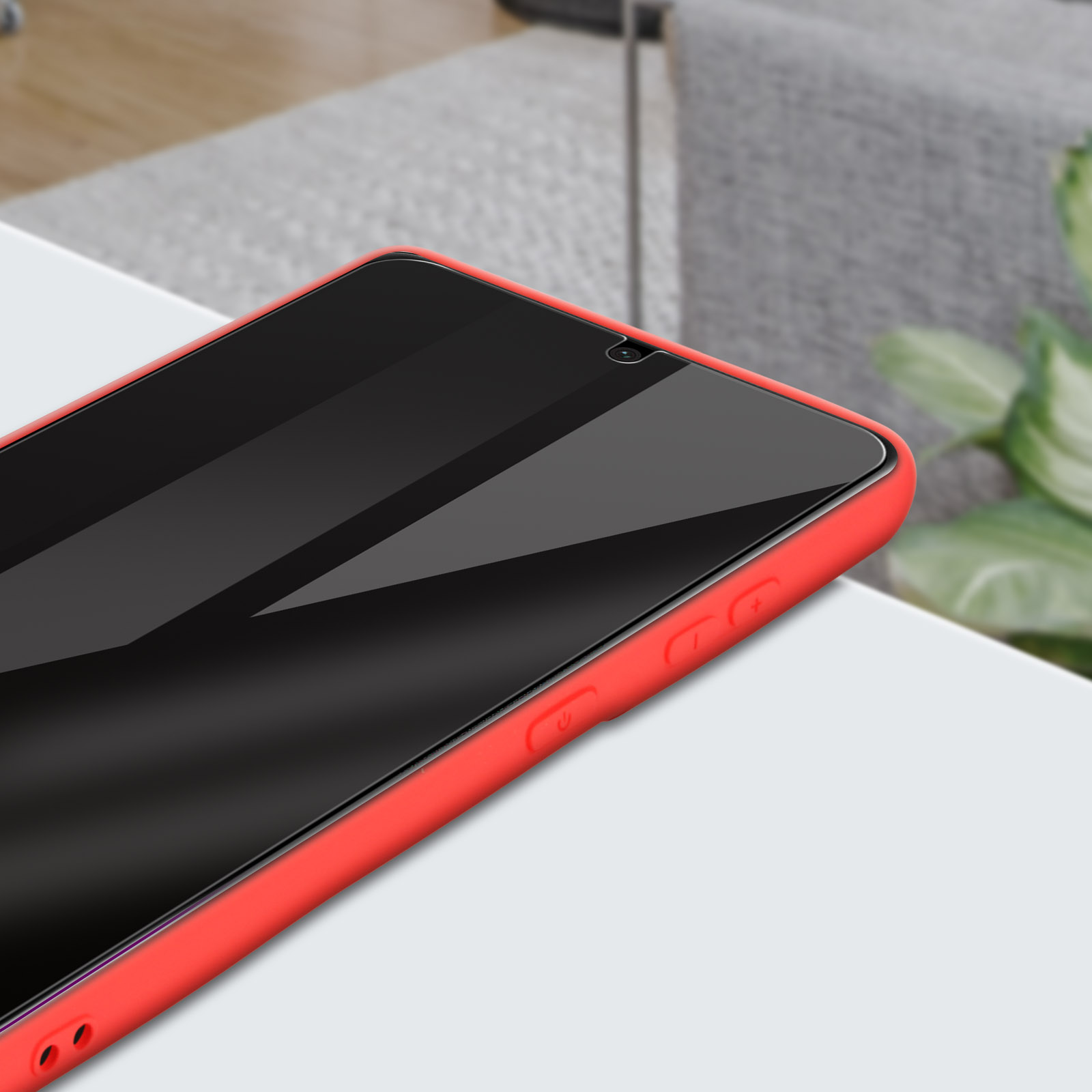 Primo piano di uno smartphone in una custodia rossa su una superficie bianca. Lo schermo è nero e riflette la luce.