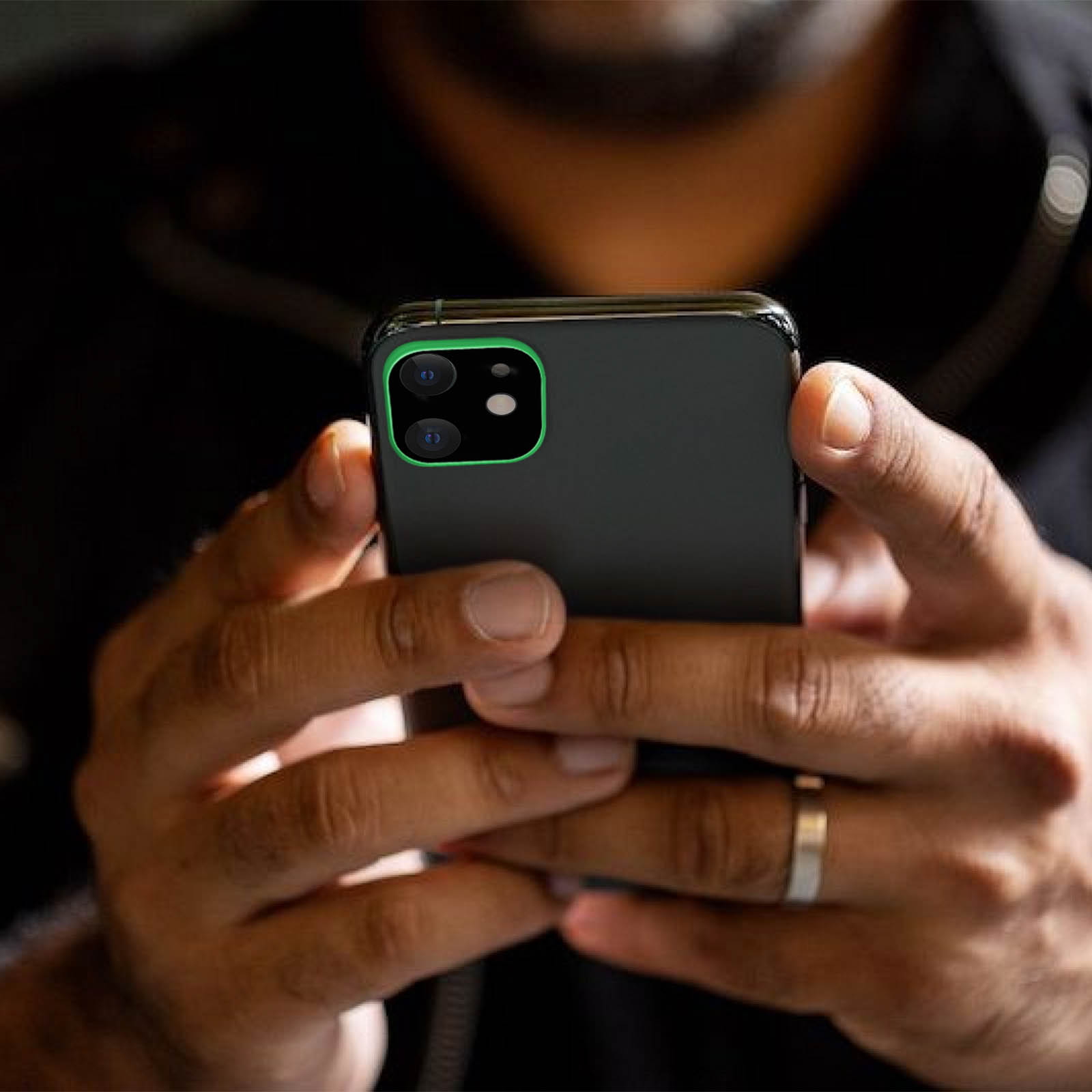 Una persona tiene in mano uno smartphone nero con una cornice verde per la fotocamera. La persona indossa un anello d'argento.