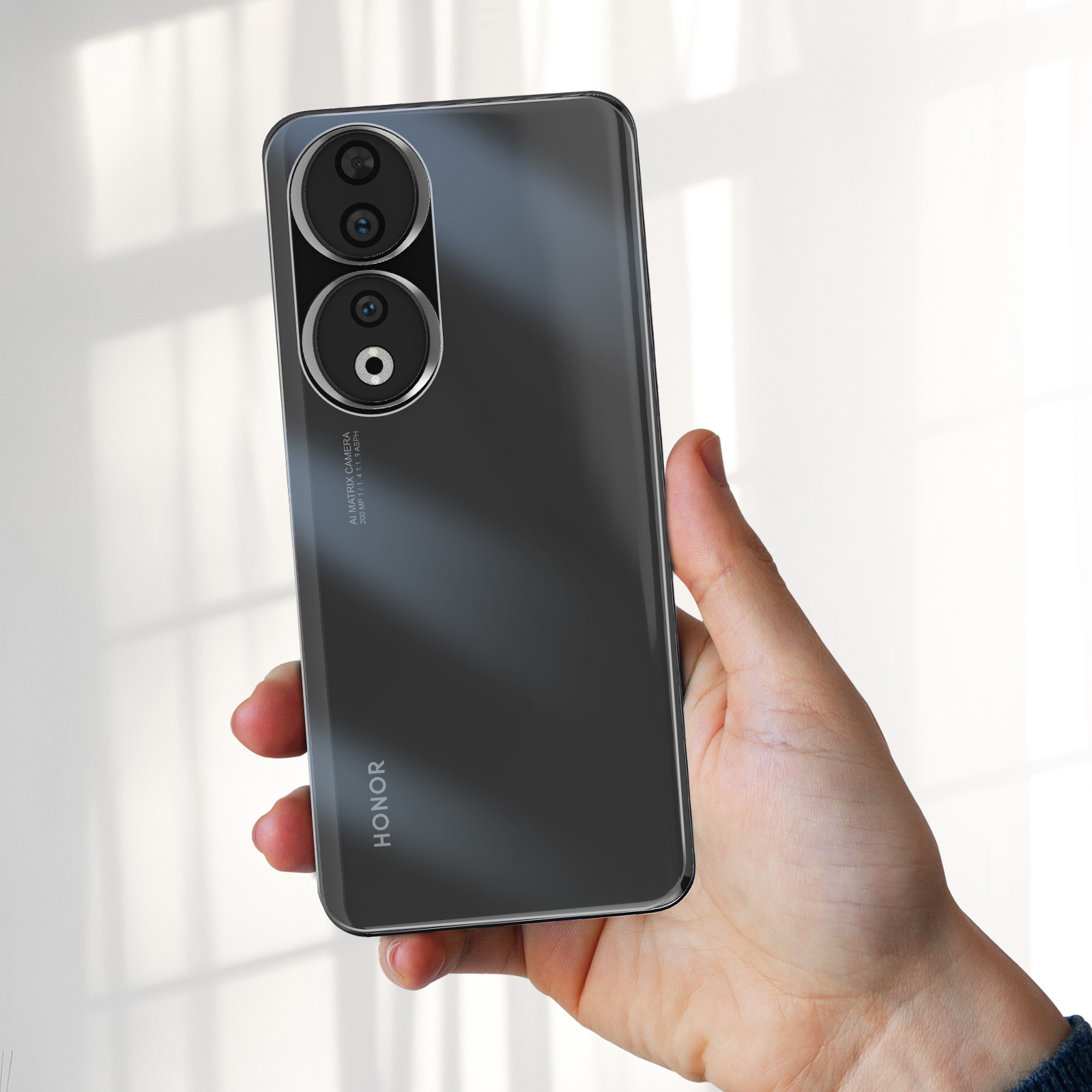 Mano che tiene un telefono Honor nero con configurazione a tripla fotocamera. Il telefono ha un retro lucido e il logo Honor è visibile.