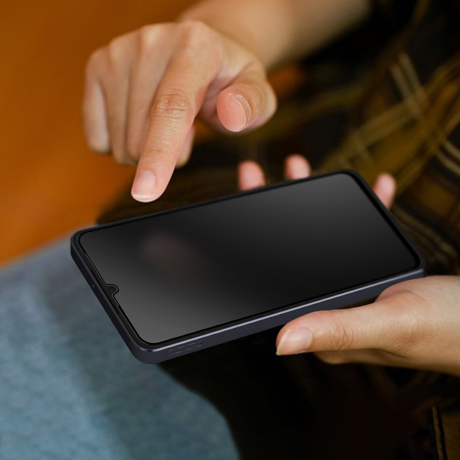 Una persona tiene in mano uno smartphone nero, con il dito puntato sullo schermo. Lo sfondo è sfocato arancione e marrone.