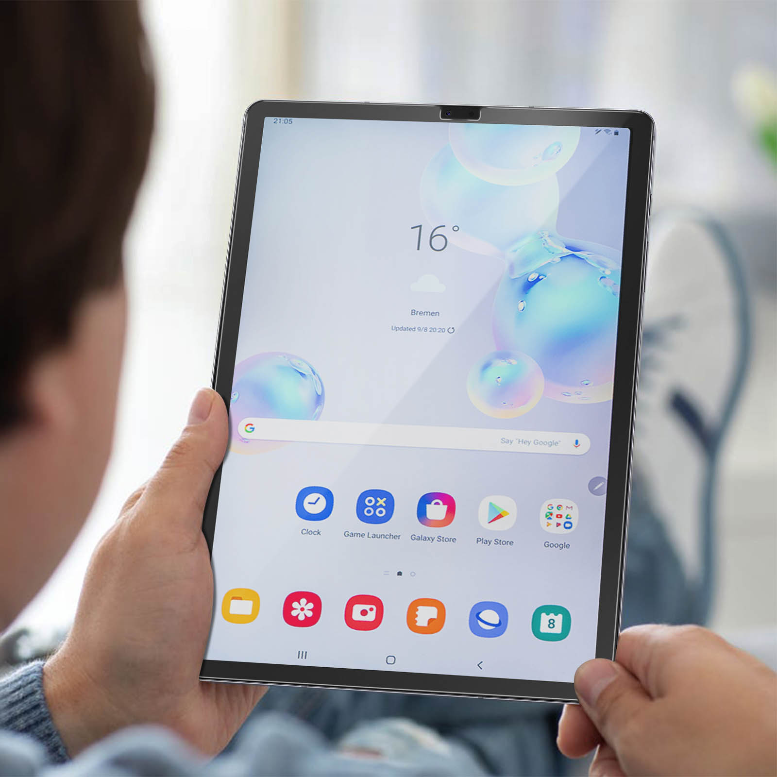 Una persona tiene in mano un tablet che mostra l'ora, la temperatura e le icone delle app. Lo schermo mostra uno sfondo blu e bianco.