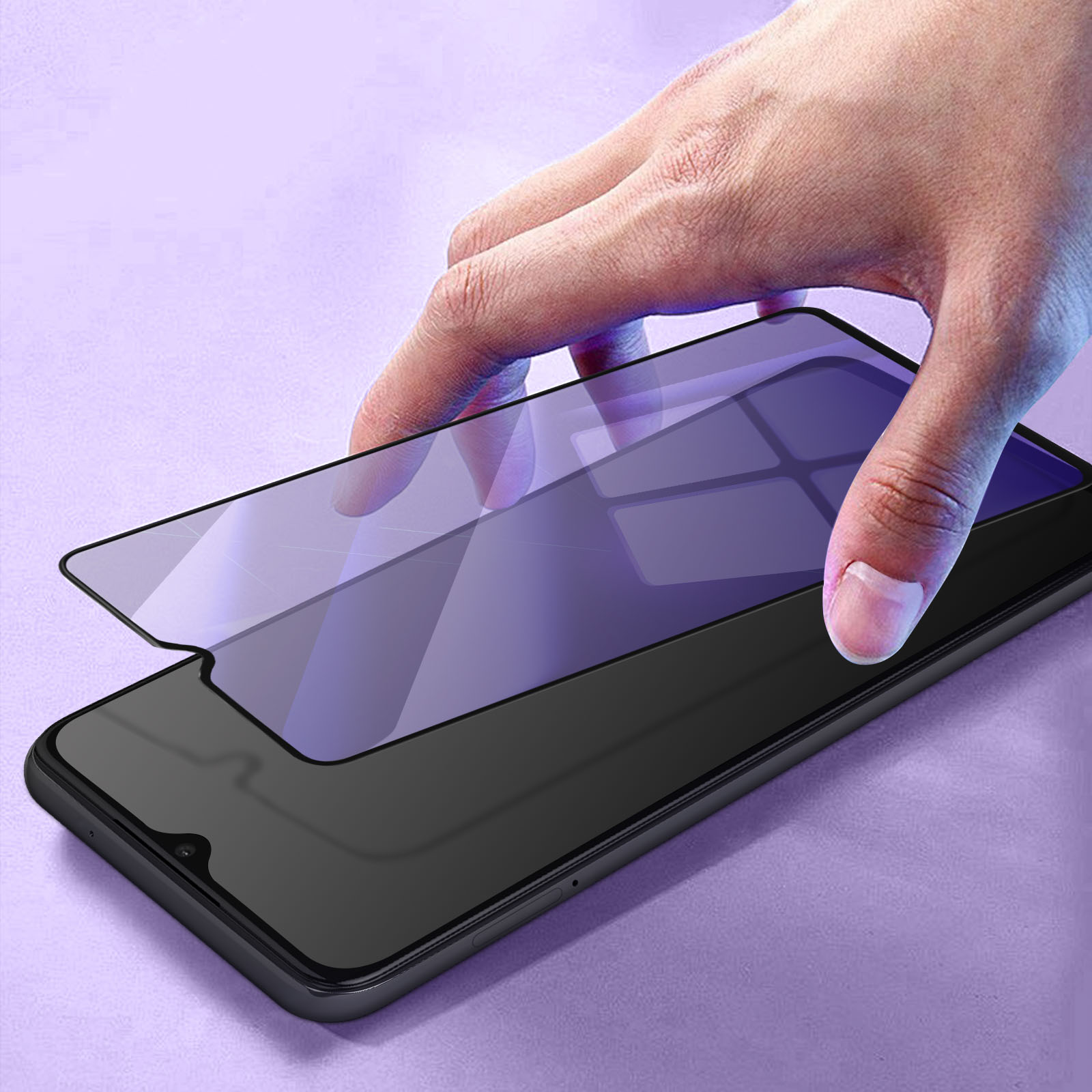 Una mano applica una protezione schermo a uno smartphone nero su una superficie viola.