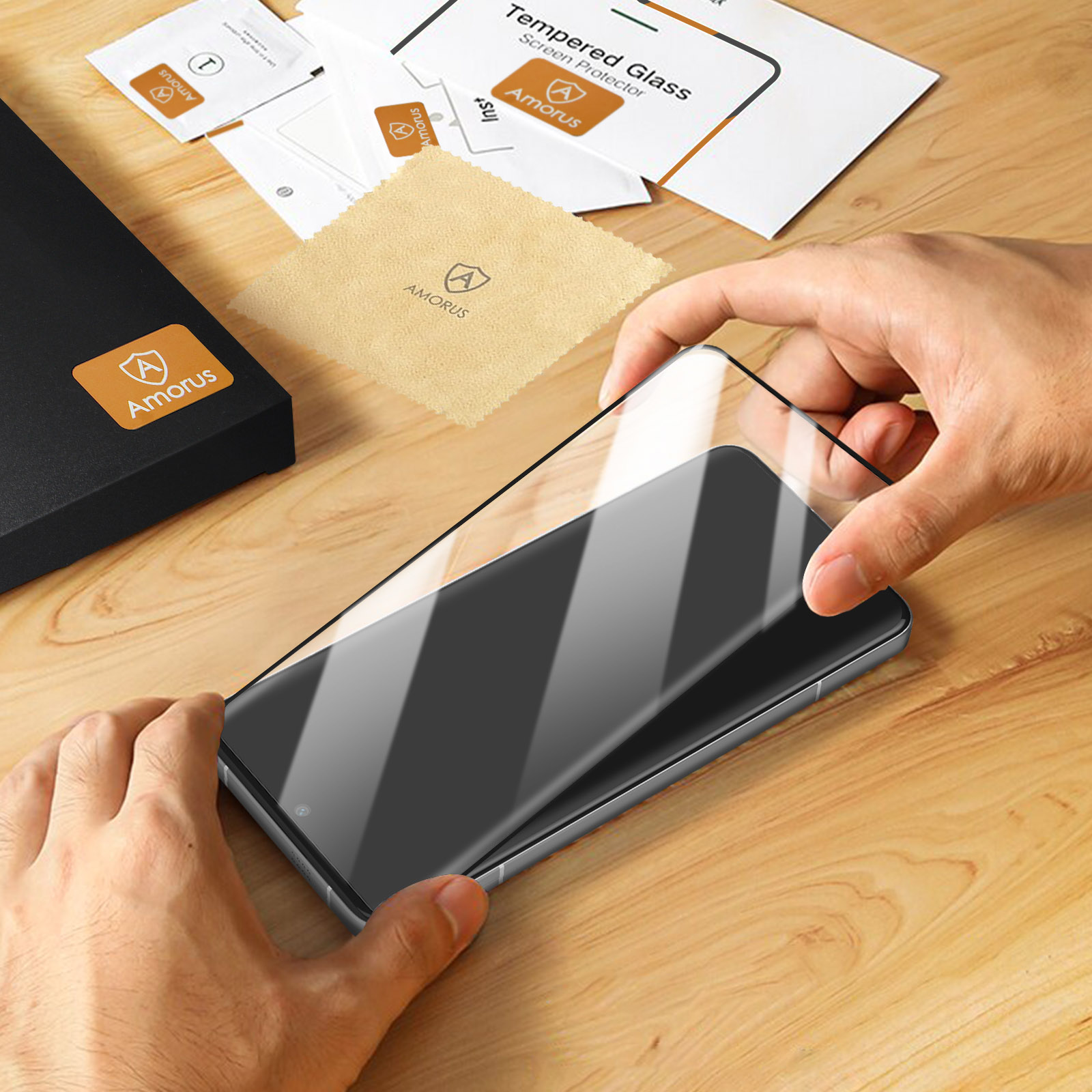 Mani che applicano una protezione per schermo in vetro temperato su un telefono. Imballaggio e accessori sullo sfondo.