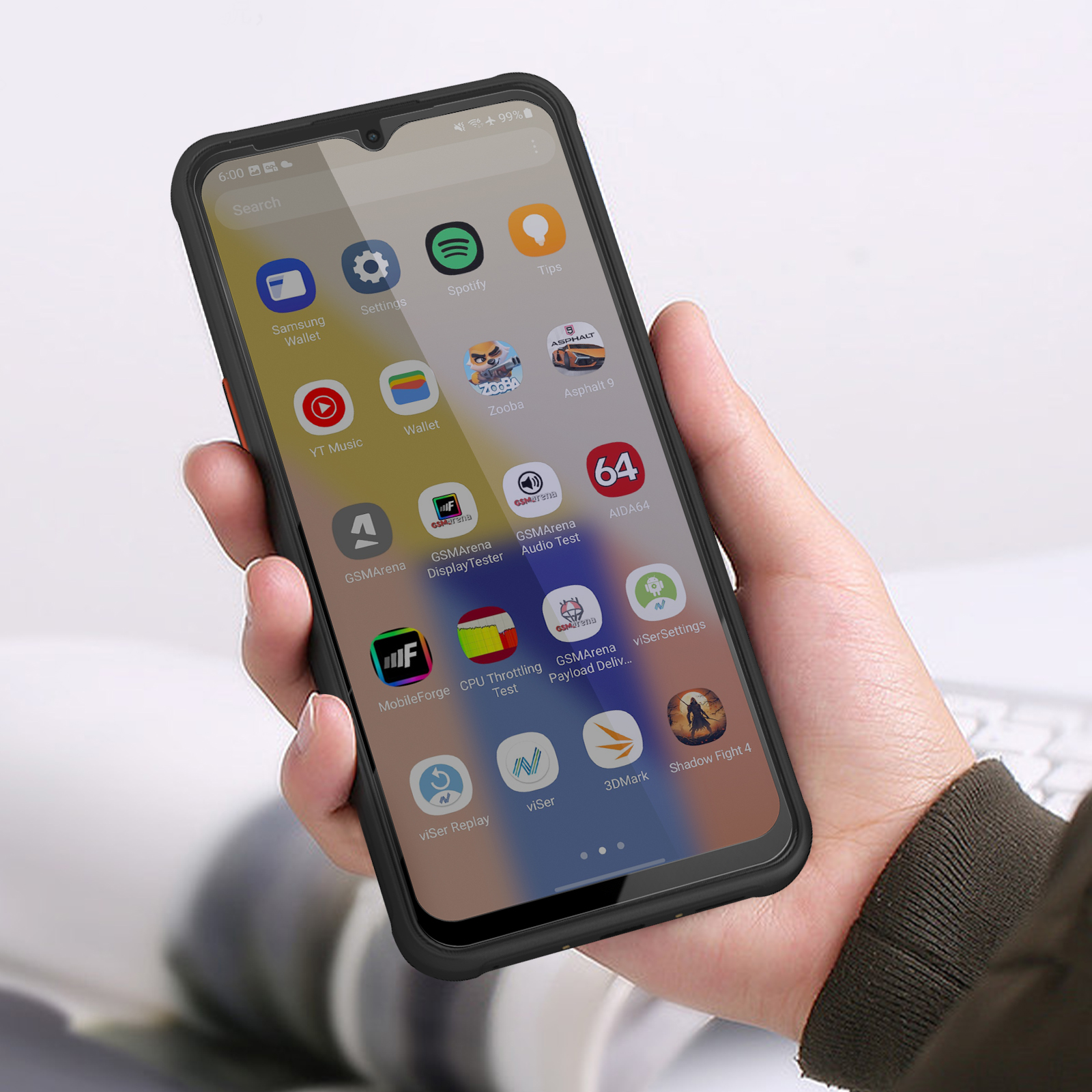 Una mano che tiene uno smartphone nero con varie icone di app sullo schermo. Lo sfondo mostra una tastiera sfocata.
